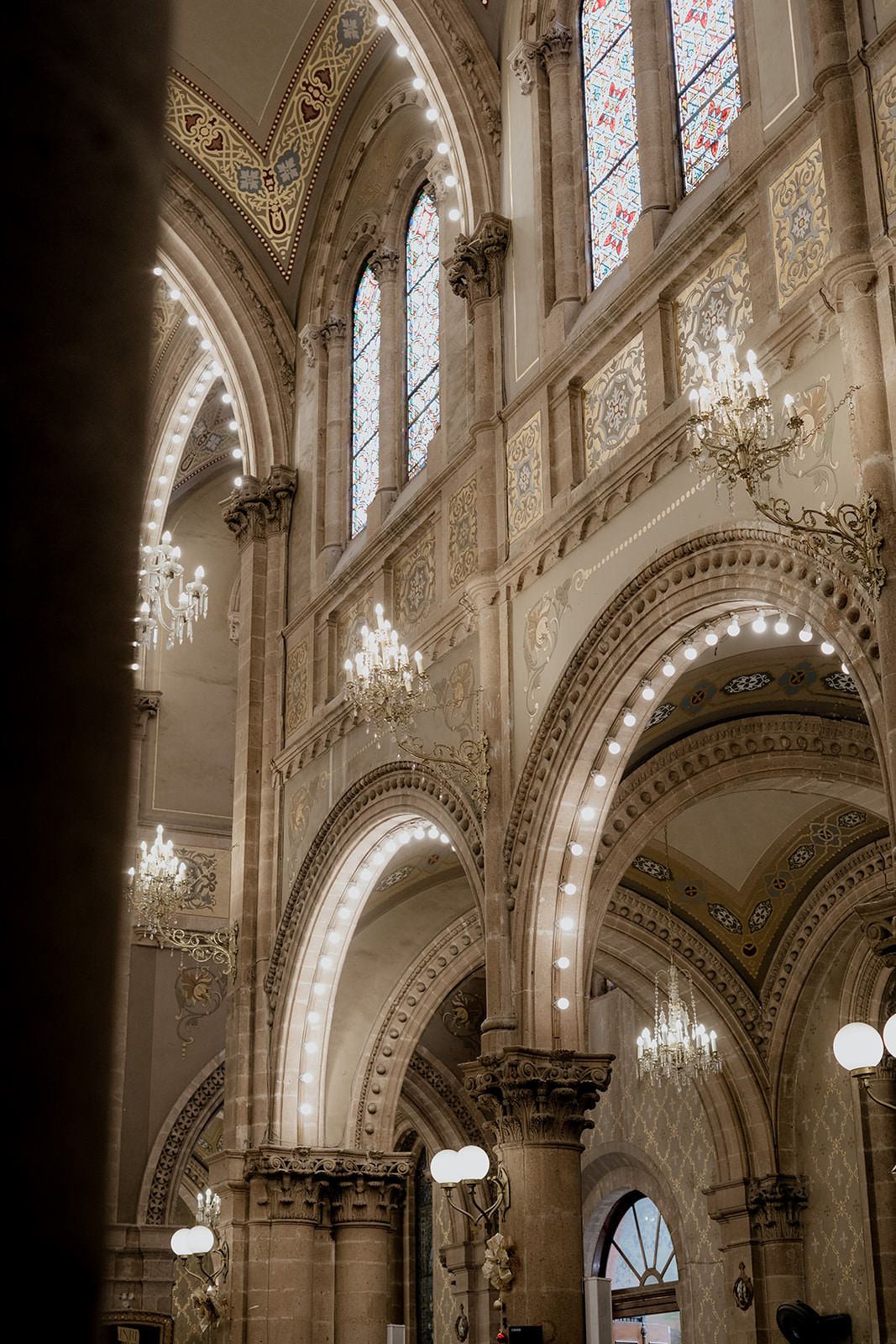 Stunning Gothic church interior with arched ceilings, crystal chandeliers, and colorful stained glass windows.