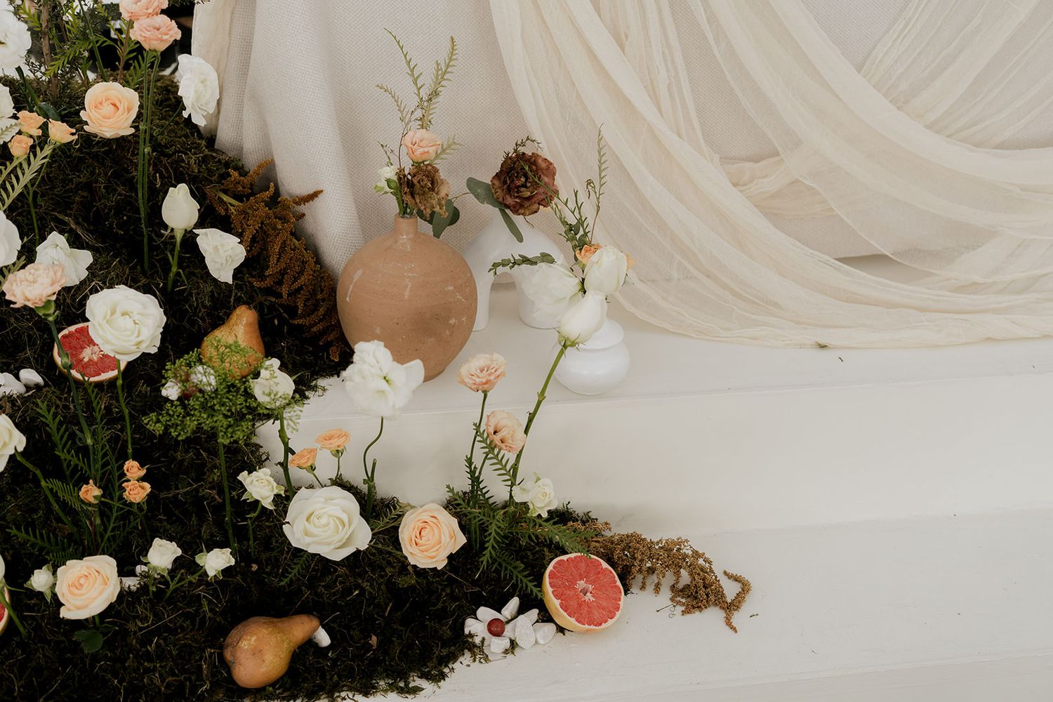 Elegant wedding floral arrangement with white and peach roses, moss, pears, and grapefruit on white steps.