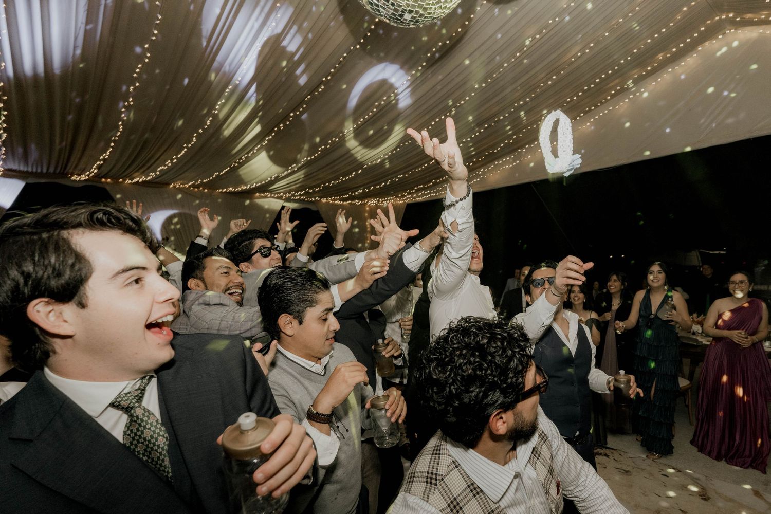 Guests dancing and celebrating at a wedding reception under sparkling disco balls and string lights.