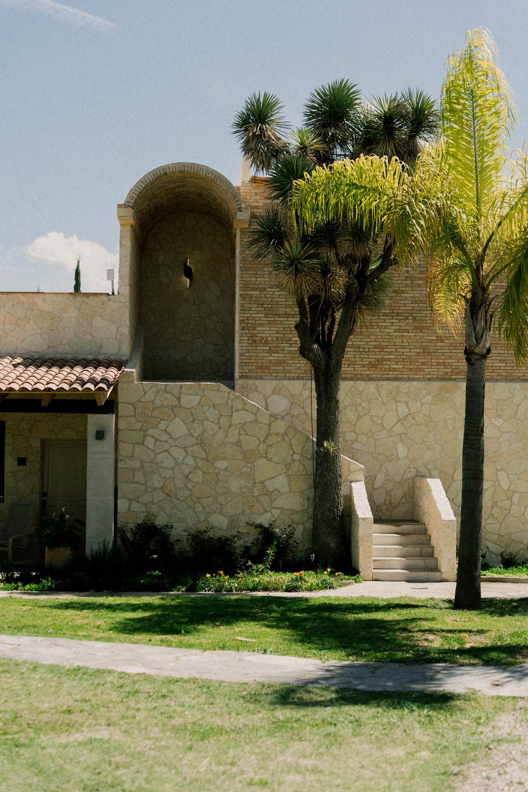 Stone wall exterior with palm trees and arched alcoves in Mediterranean architectural style.