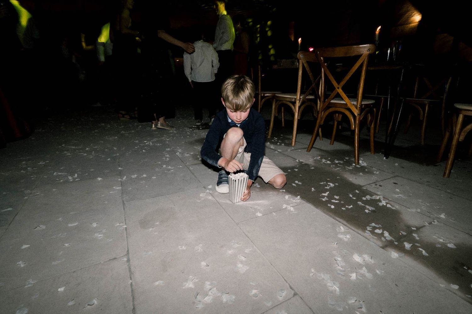 Person crouches on floor covered in white confetti at nighttime party venue.