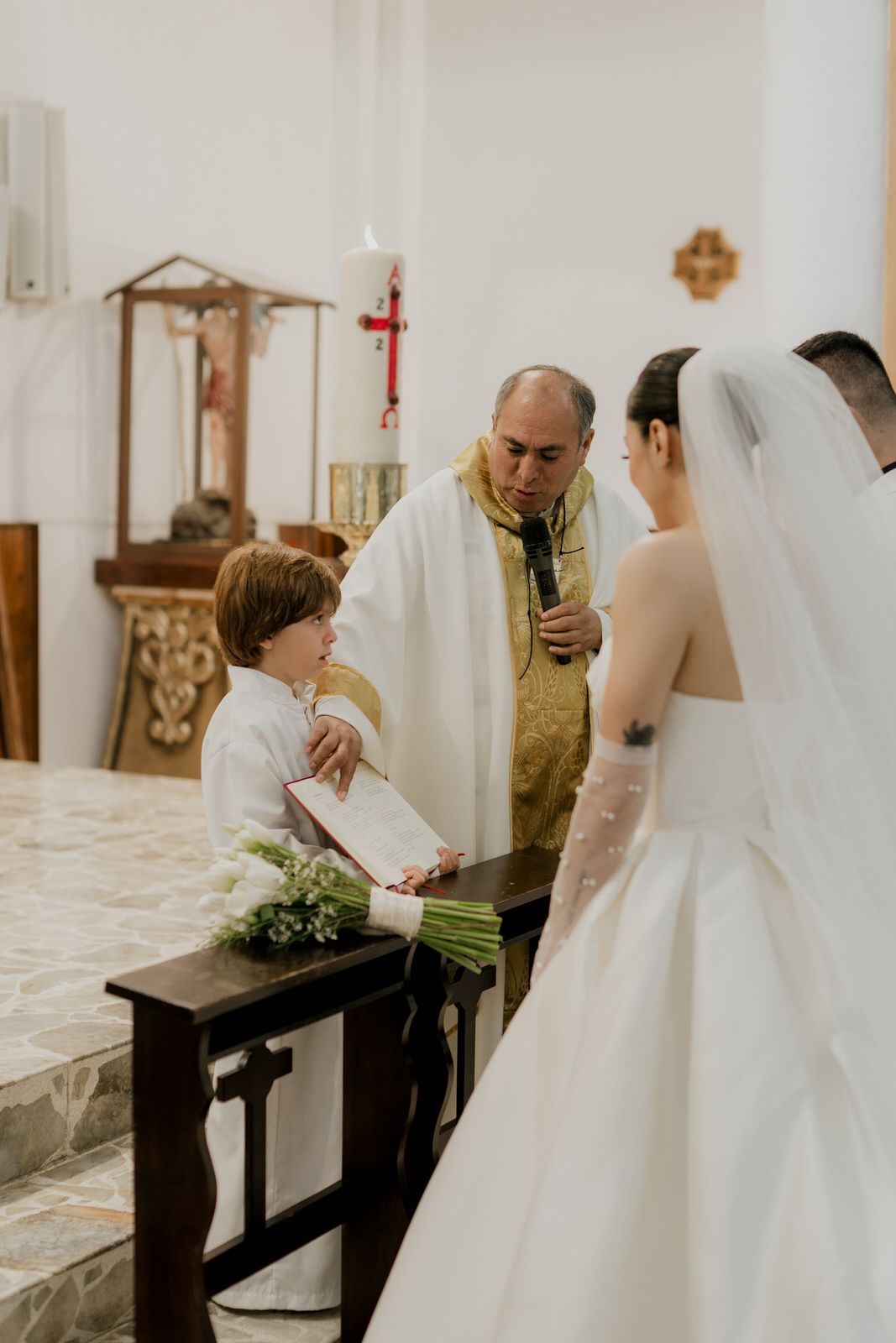 Wedding ceremony participants stand near wooden pews in an ornate church interior.