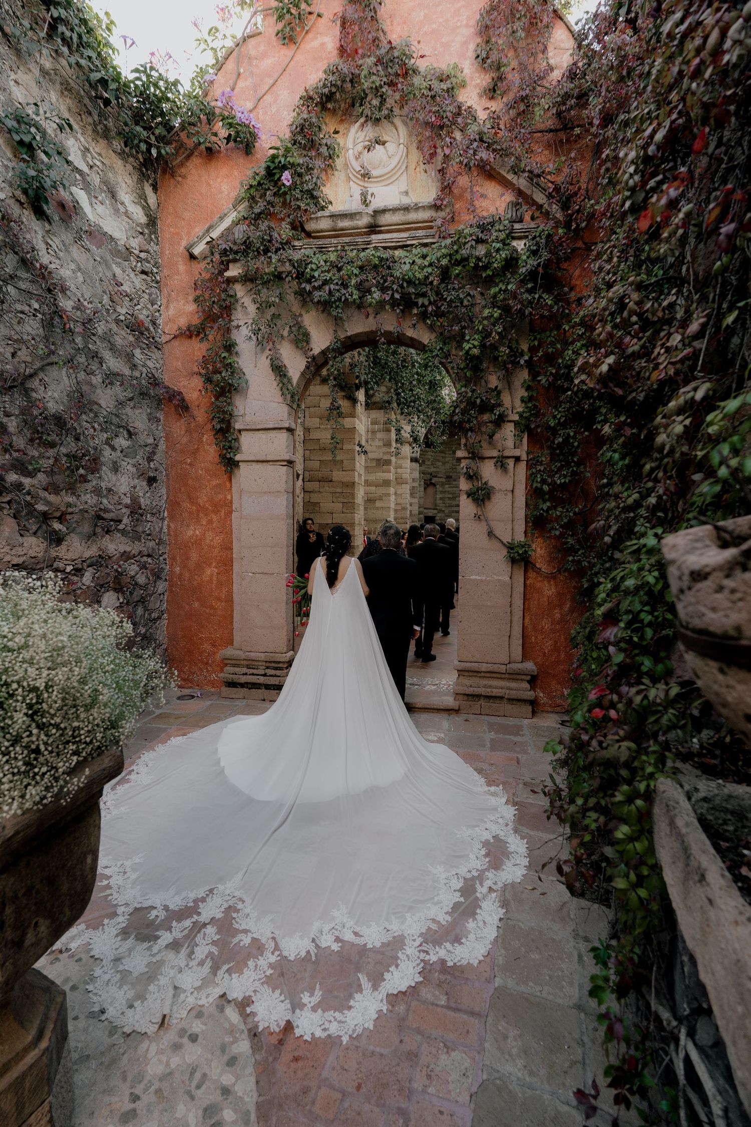 Wedding dress train trailing along rustic stone pathway with ivy covered walls.