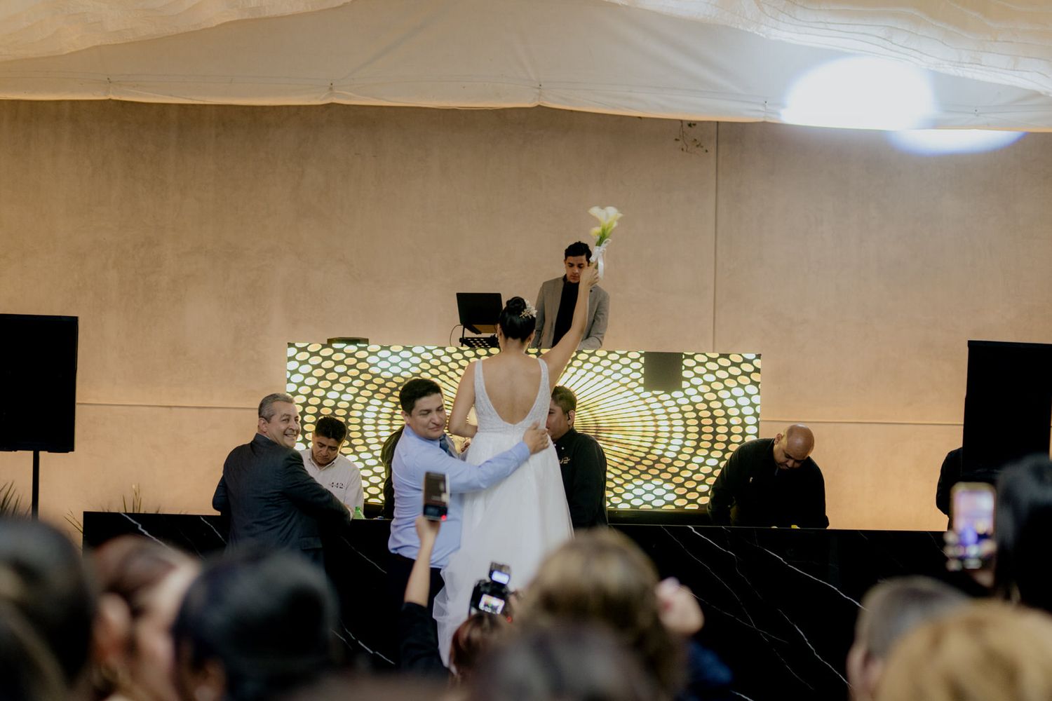 Bride and groom share a dance on stage at their wedding reception with guests watching.