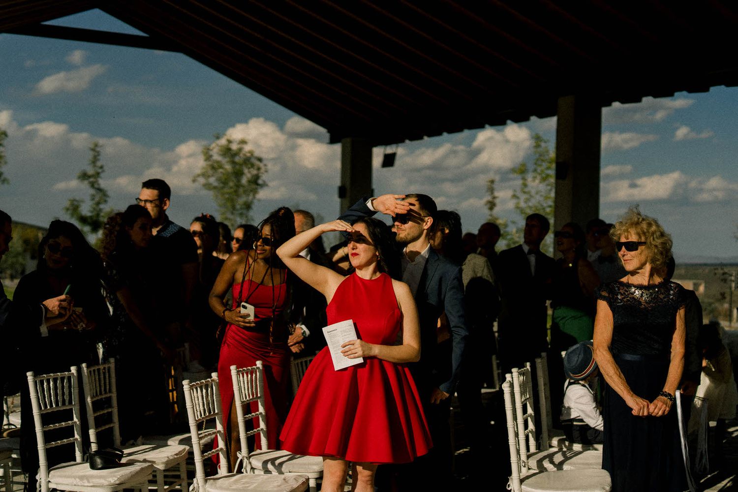 Wedding guests gathered under shaded outdoor venue during daytime celebration.