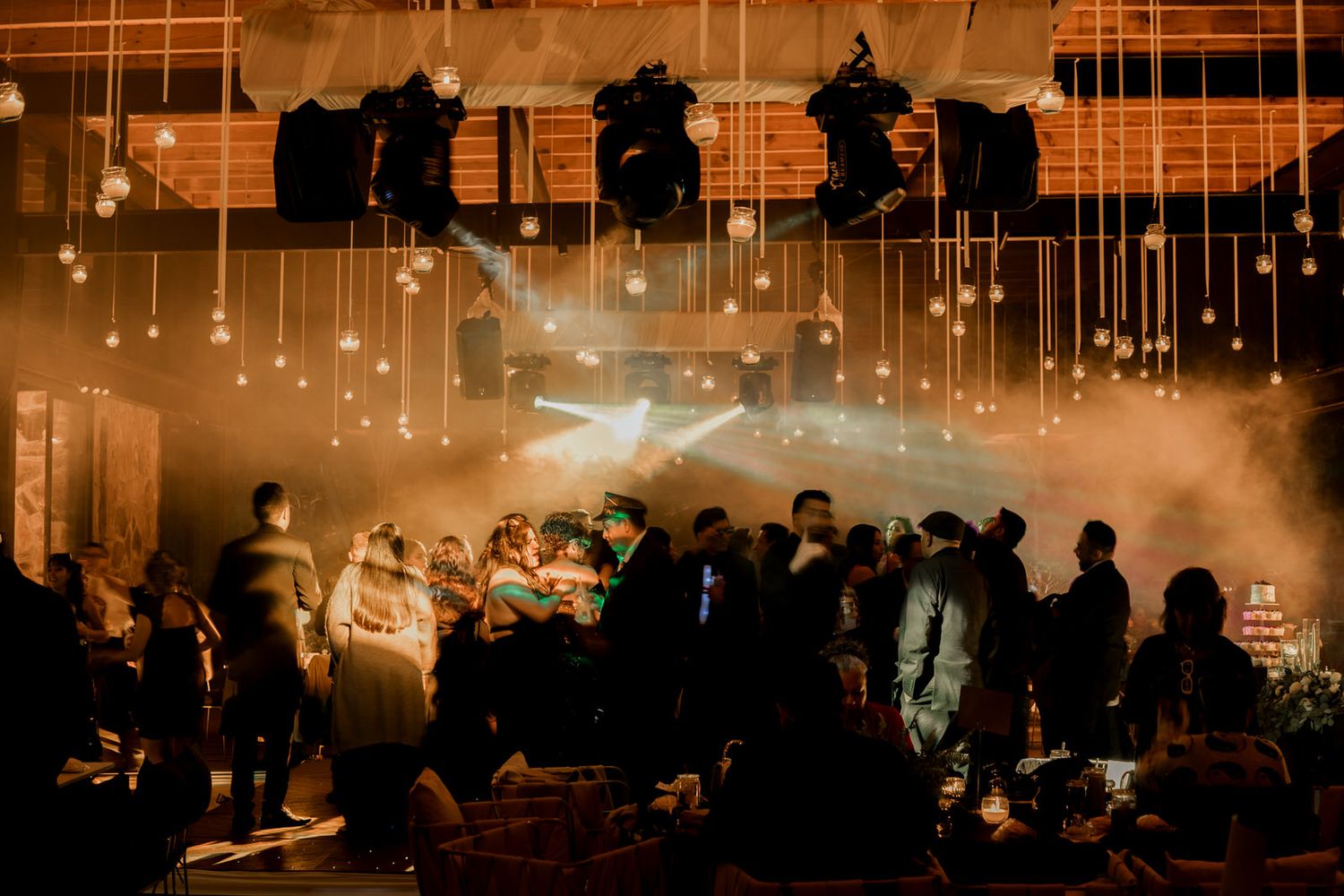 Warm lighting illuminates a festive indoor venue with hanging string lights and dancing guests.