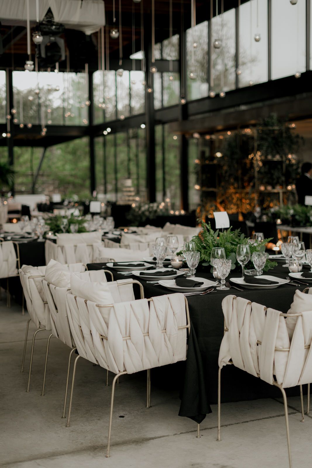 Modern wedding reception venue with white chairs and black tablecloths in an industrial-style space.