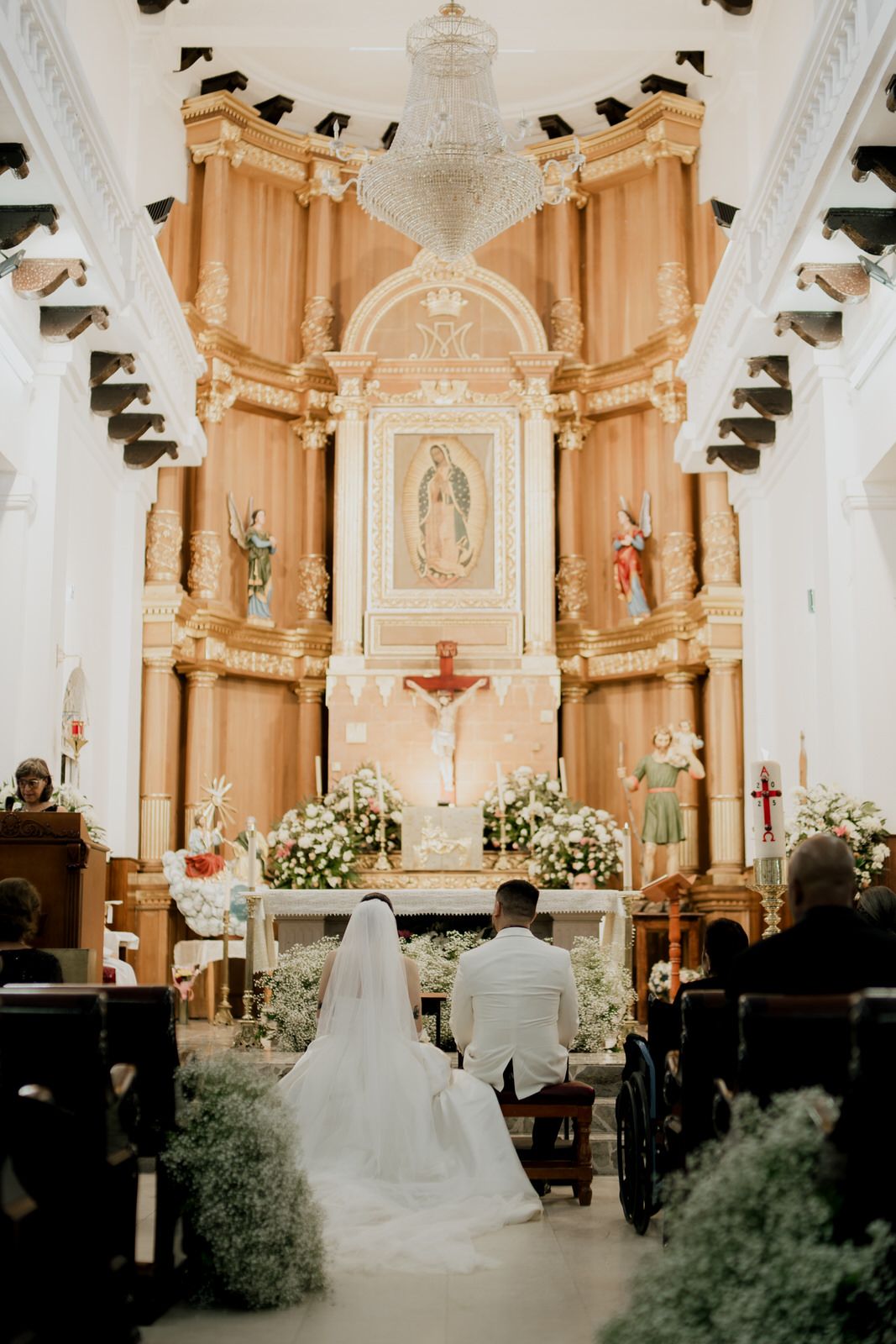 An ornate church altar decorated with white flowers and a crucifix during a wedding ceremony.
