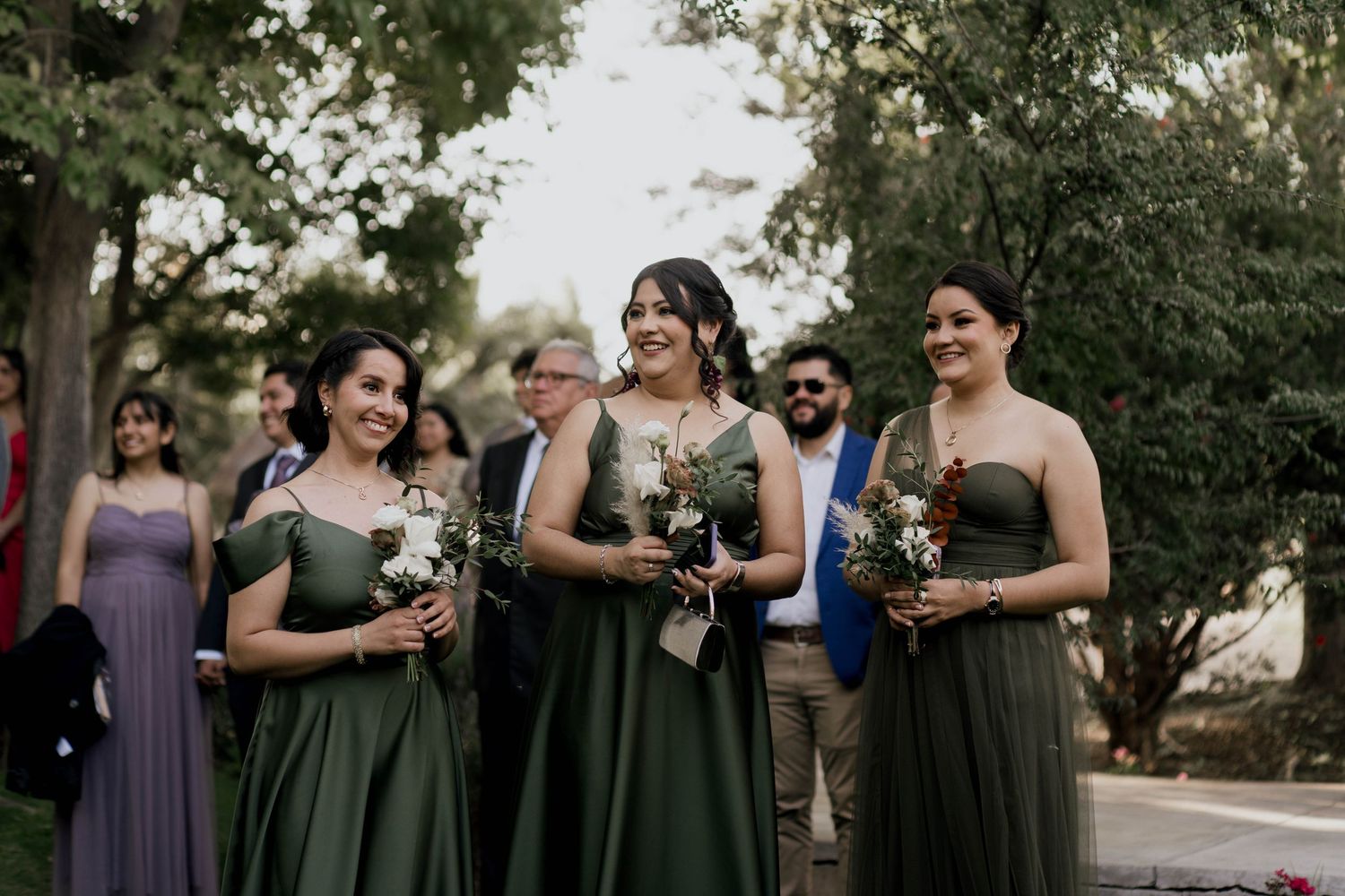 Bridesmaids in purple and olive green dresses pose together at an outdoor wedding ceremony.