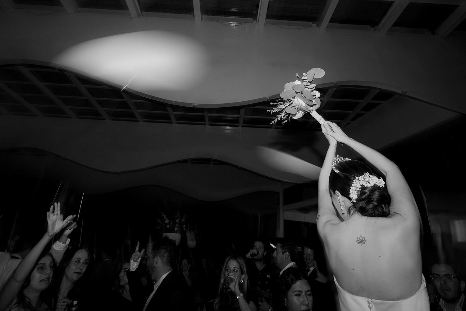 Bride tossing bouquet to eager guests at wedding reception in black and white photo.