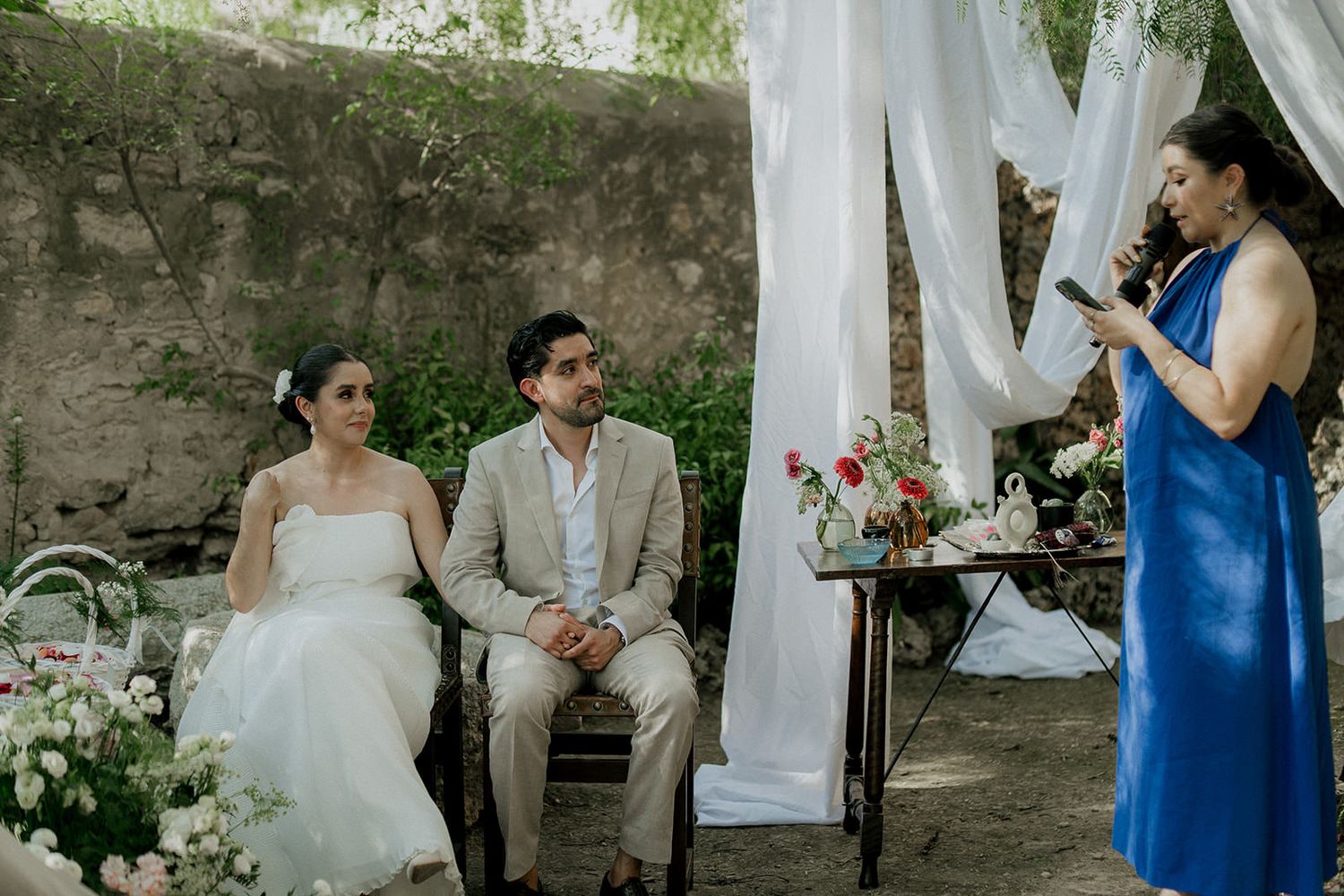 Garden wedding setup with white fabric draping and stone wall backdrop.