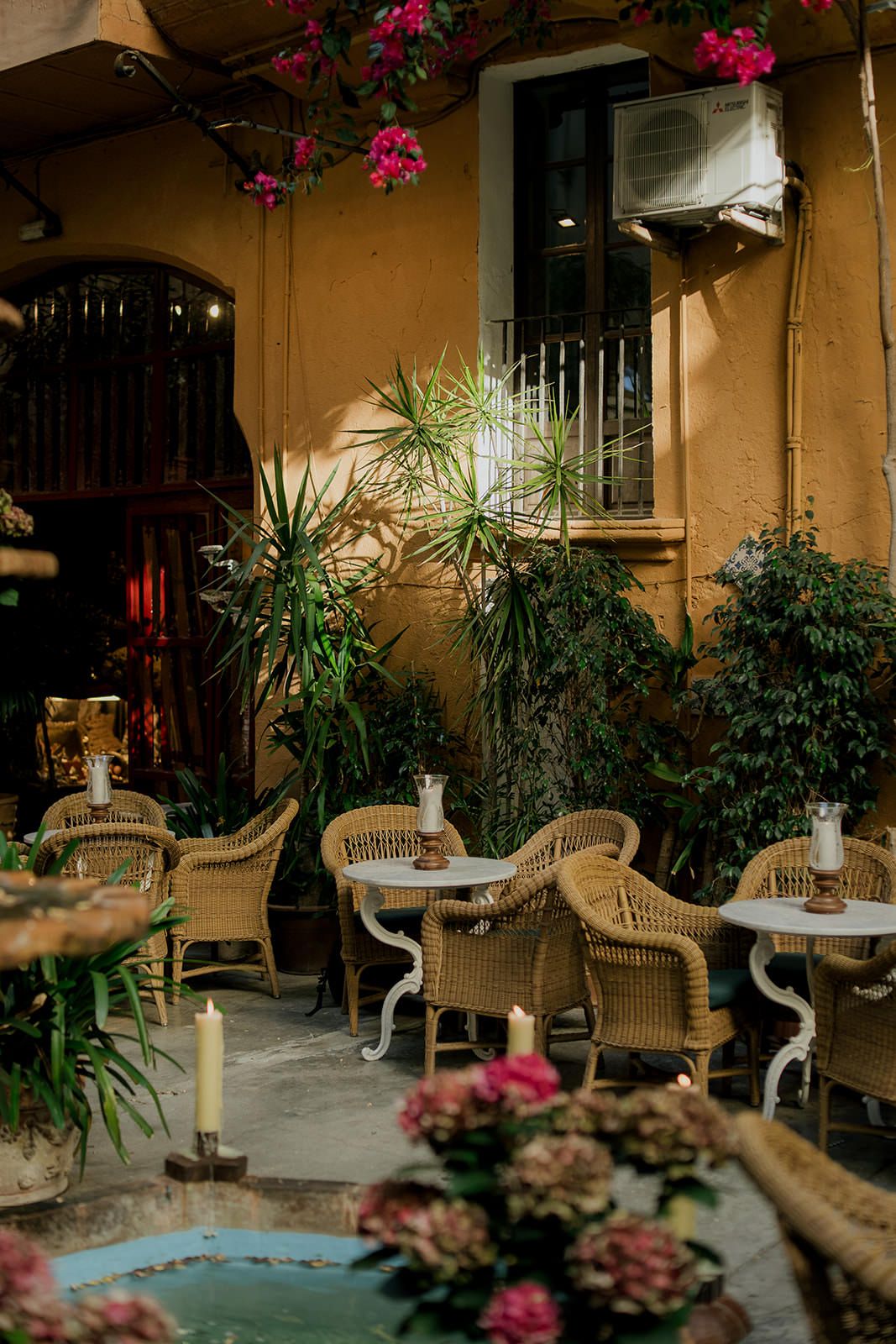 Mediterranean courtyard cafe with wicker furniture and blooming bougainvillea flowers in warm evening light.