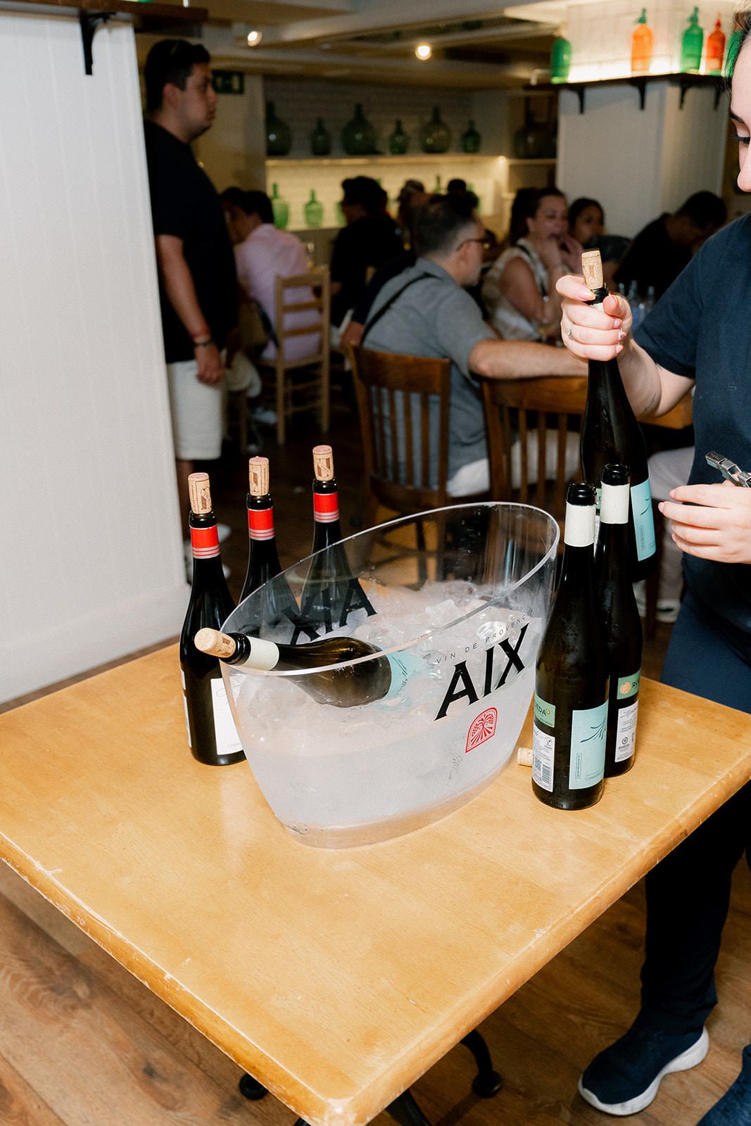 Wine bottles and ice buckets arranged on wooden tables in a casual dining setting.