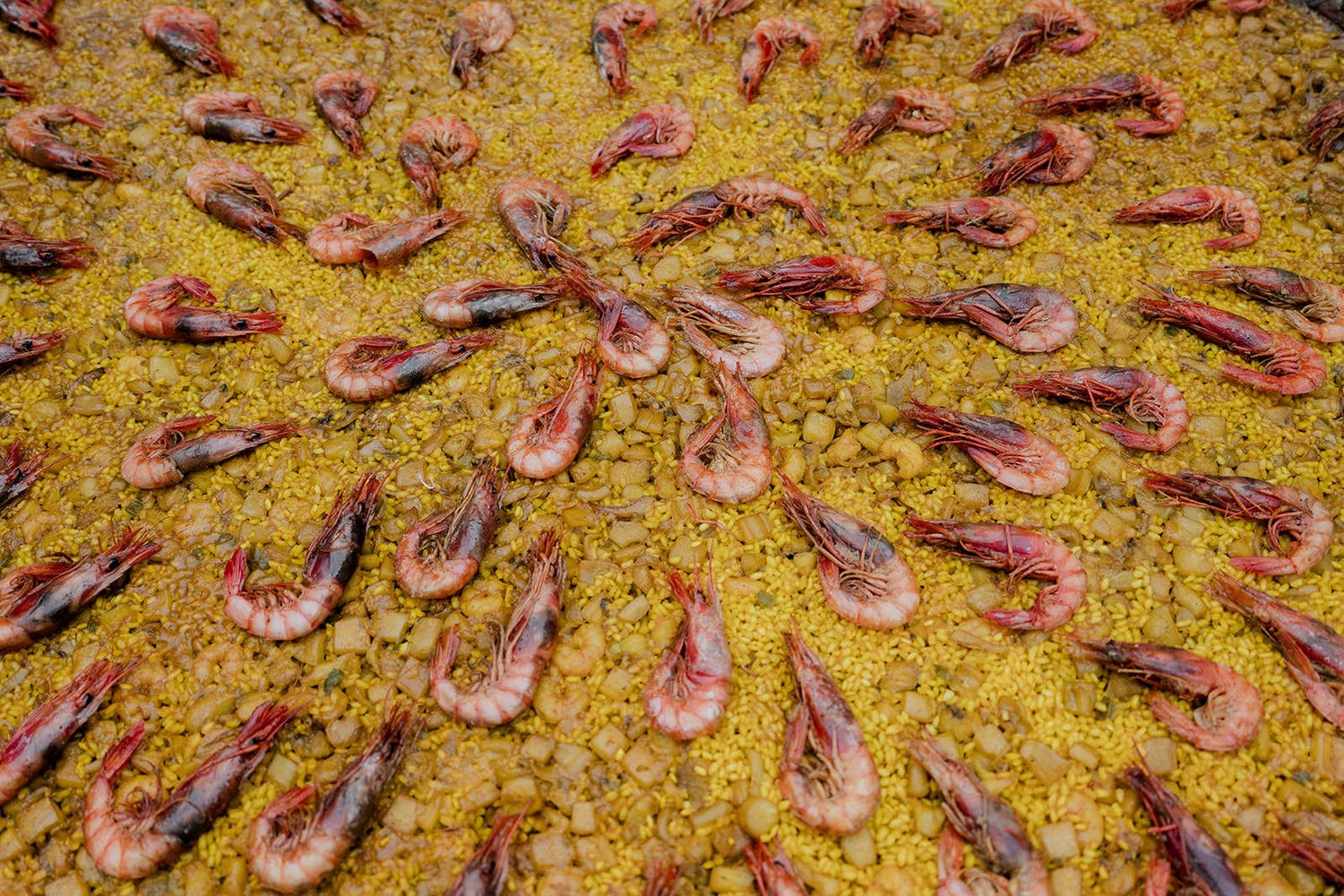 Close-up of a golden Spanish paella with shrimp and saffron rice arranged in a decorative pattern.