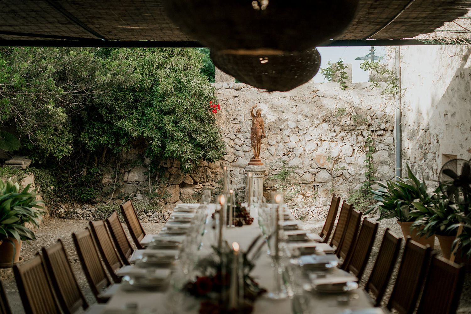 Long wooden tables set up for an elegant outdoor wedding reception in a rustic stone courtyard.