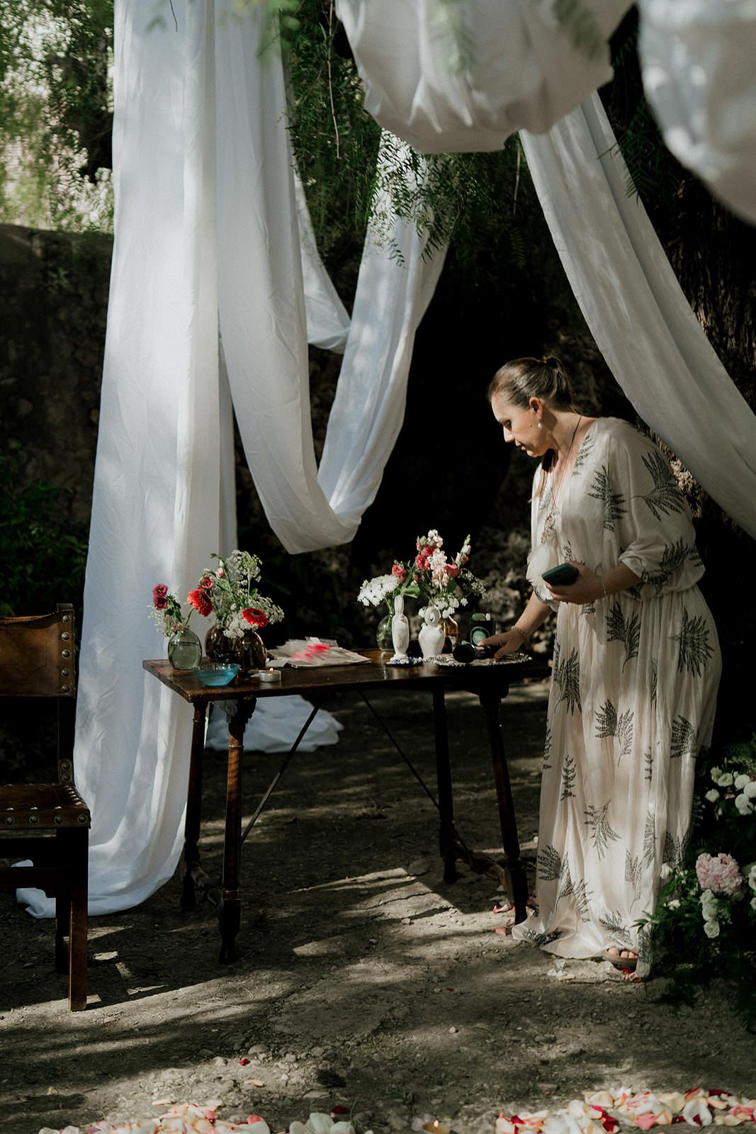 Ethereal outdoor wedding scene with flowing white drapes and rustic wooden table decorated with floral arrangements.