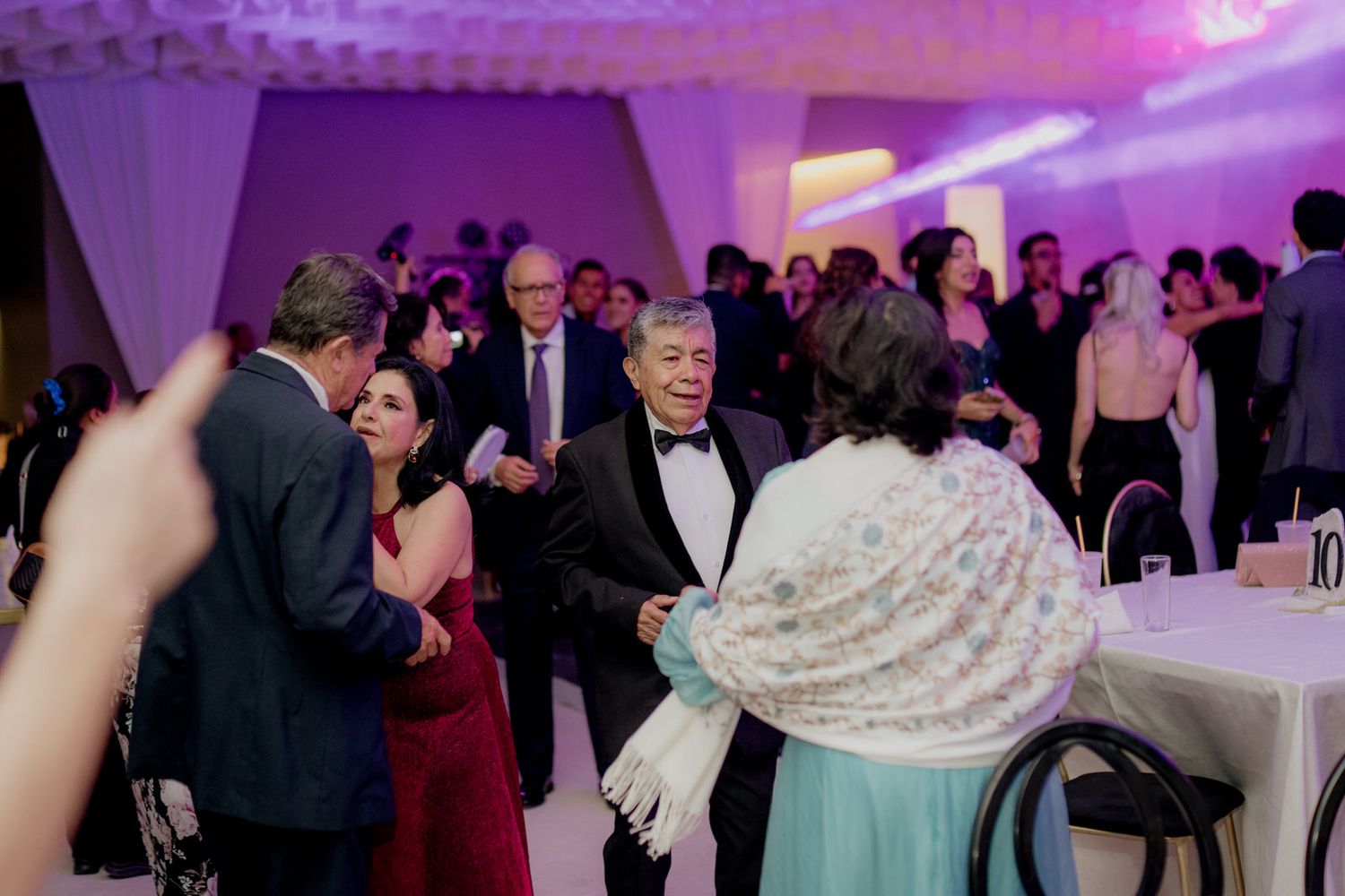 Wedding guests dancing and socializing under purple lights at a festive reception.