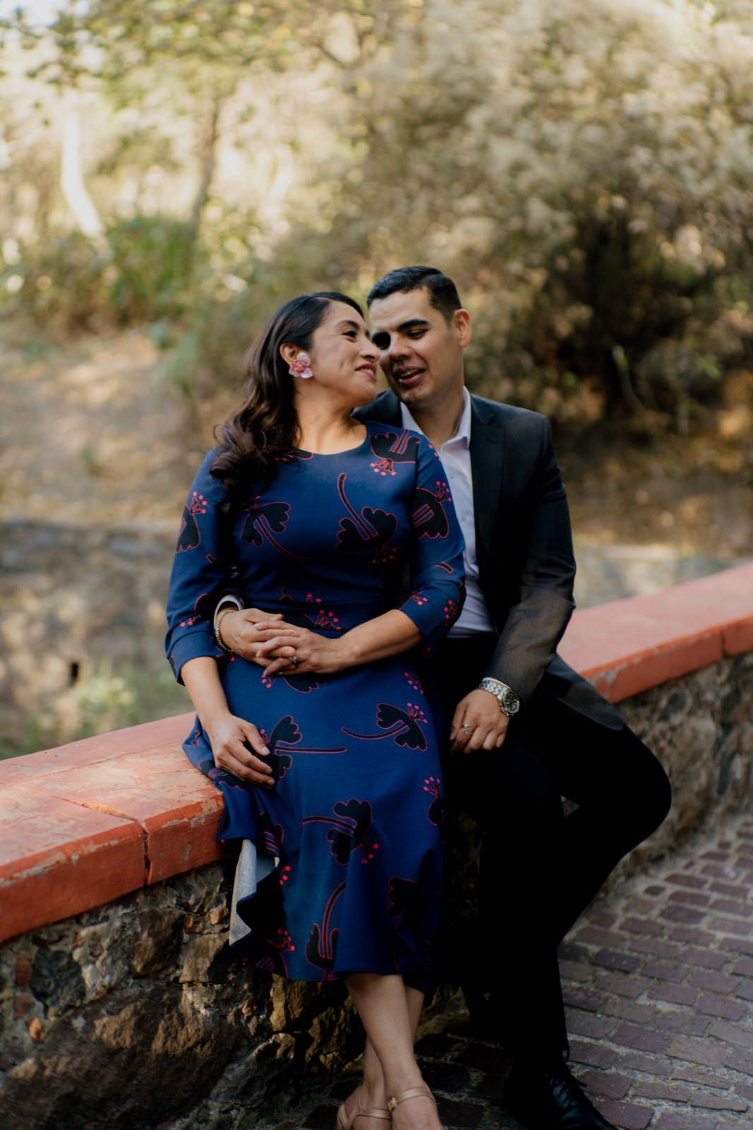 Couple sharing an intimate moment while sitting on a brick wall in a garden setting.