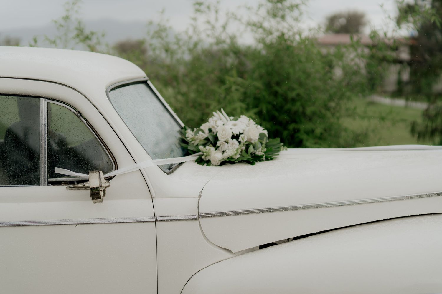 Detail shot of a pristine white vintage car at an outdoor wedding venue.