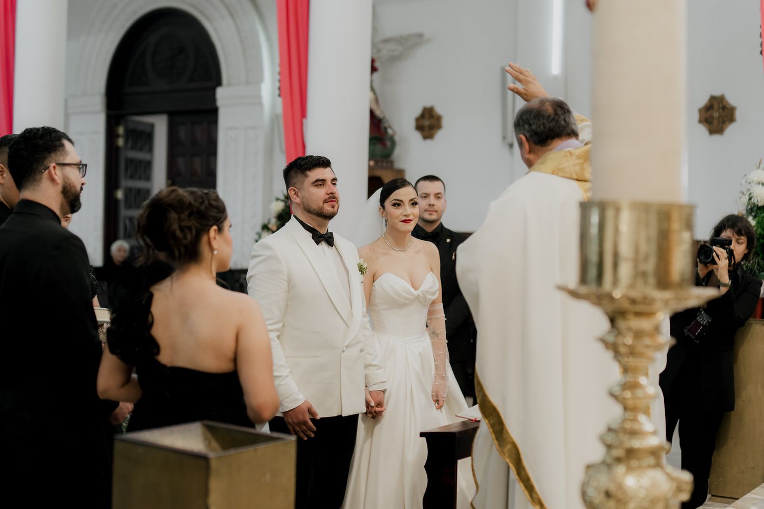 Wedding ceremony in progress inside a traditional church with red accents and golden candlesticks.