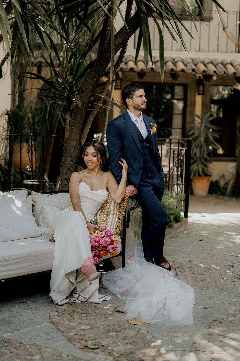 Bride and groom share intimate moments while sitting on a bench in a garden courtyard during their wedding photoshoot.