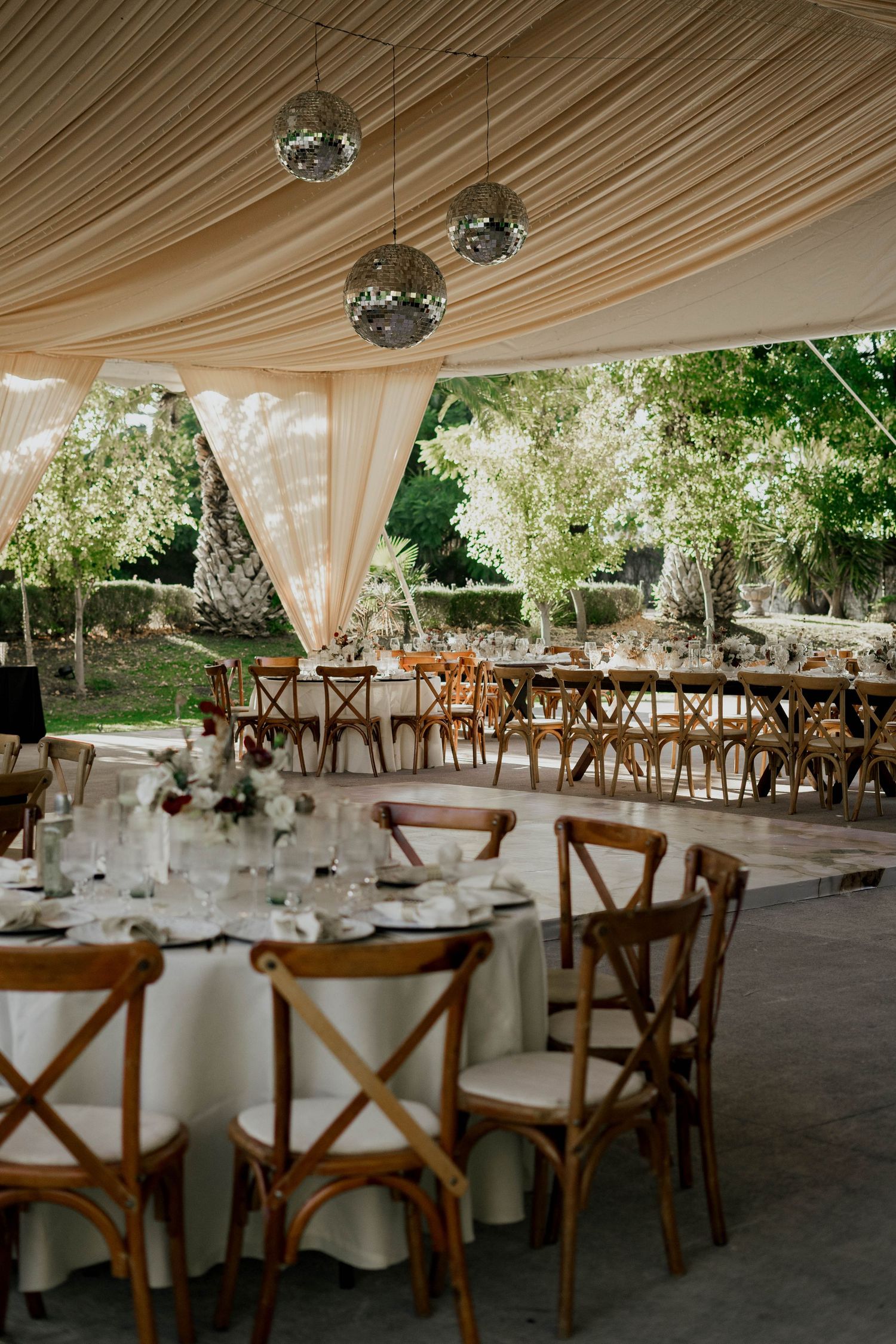 Wedding reception venue with draped ceiling, wooden crossback chairs, and round tables.