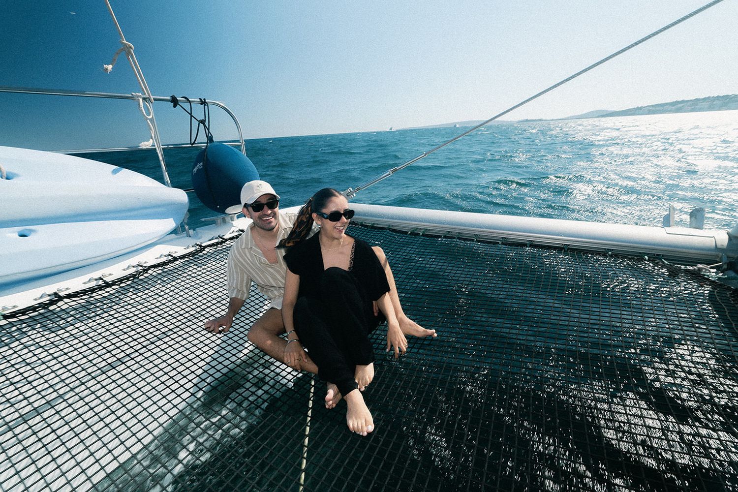 Passengers lounging on the netting of a sailing catamaran while cruising across turquoise waters.