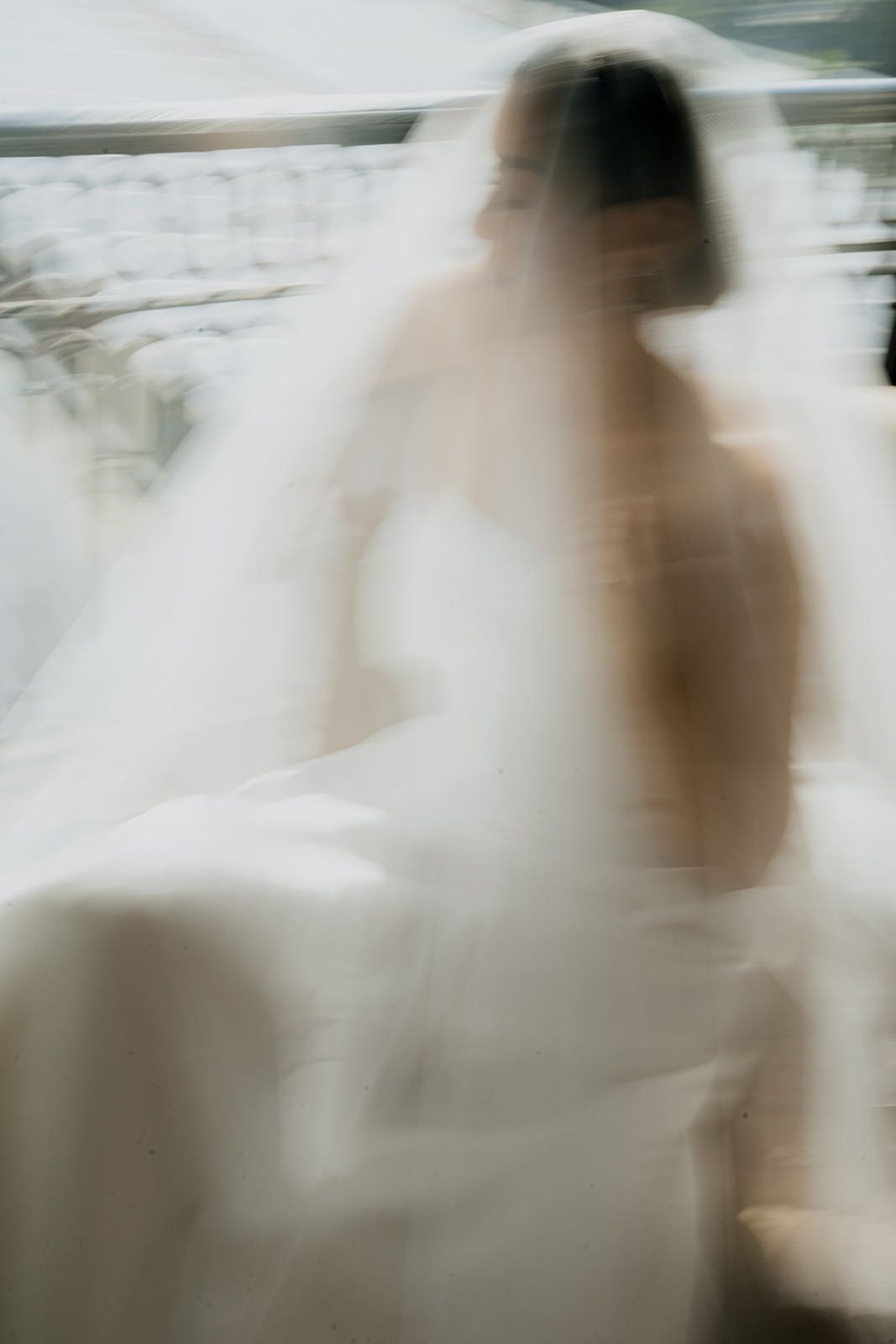 Artistic motion blur portrait of bride in white wedding dress and veil walking.