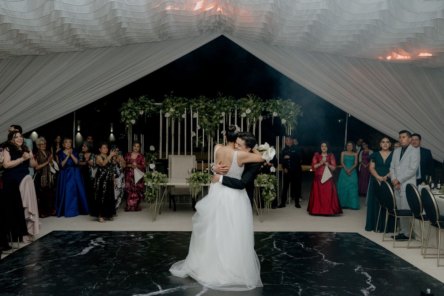 Bride and groom share their first dance in an elegant wedding reception venue with draped ceilings and floral decor.