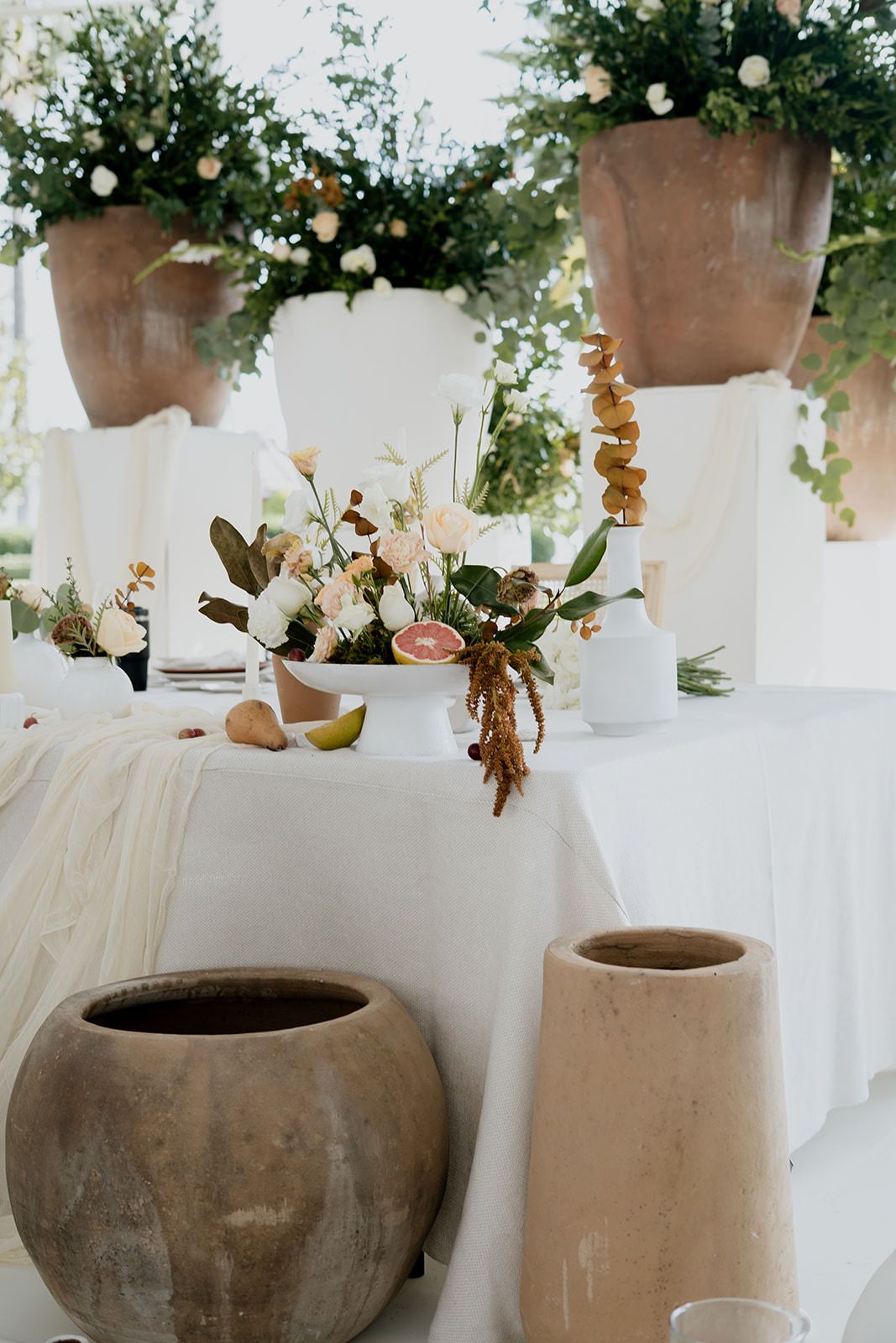 Elegant wedding reception table with white linens, floral arrangements, and rustic terracotta pots.