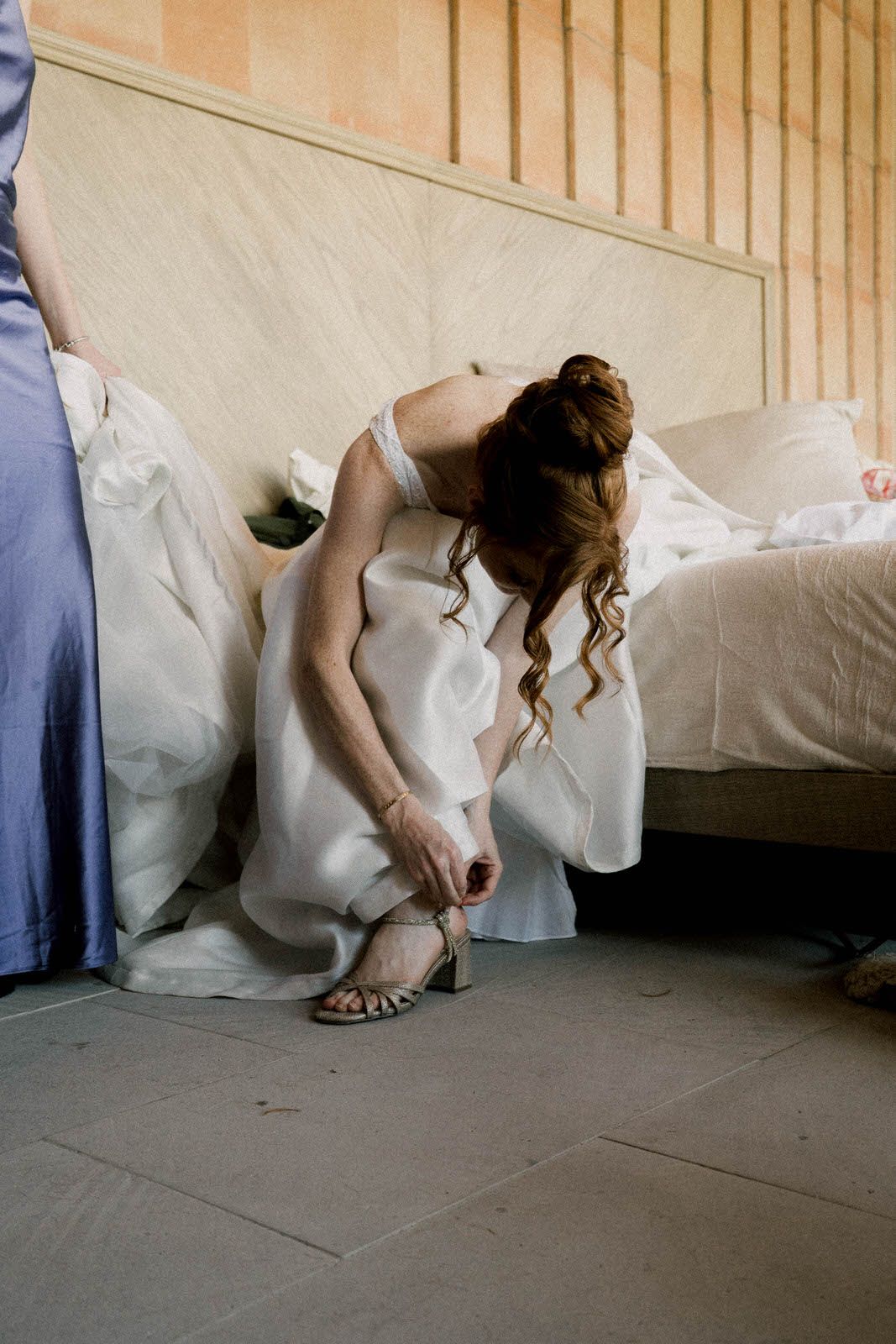 Person in white dress adjusting shoes on tiled floor.