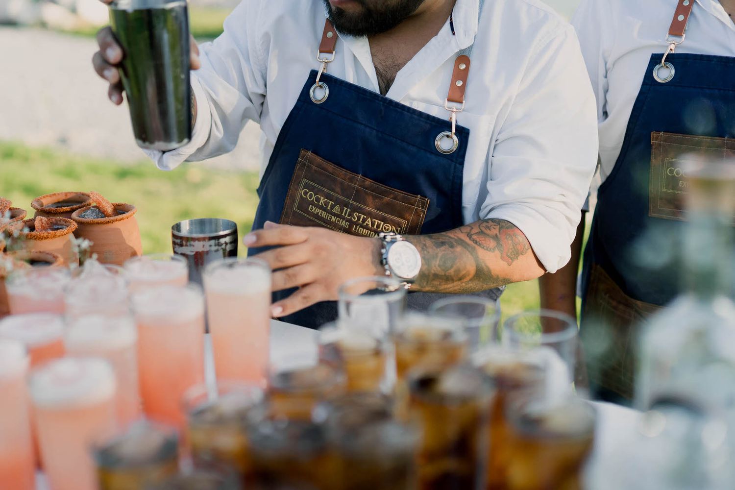 Bartenders in white uniforms preparing drinks at an outdoor event bar.