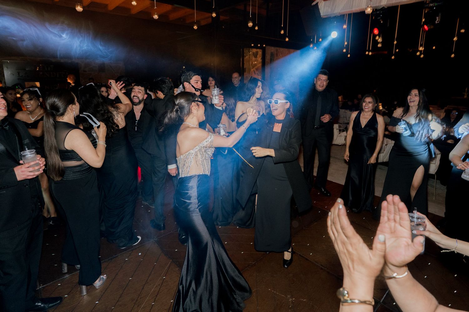 Partygoers dancing beneath blue spotlights at a nighttime celebration.