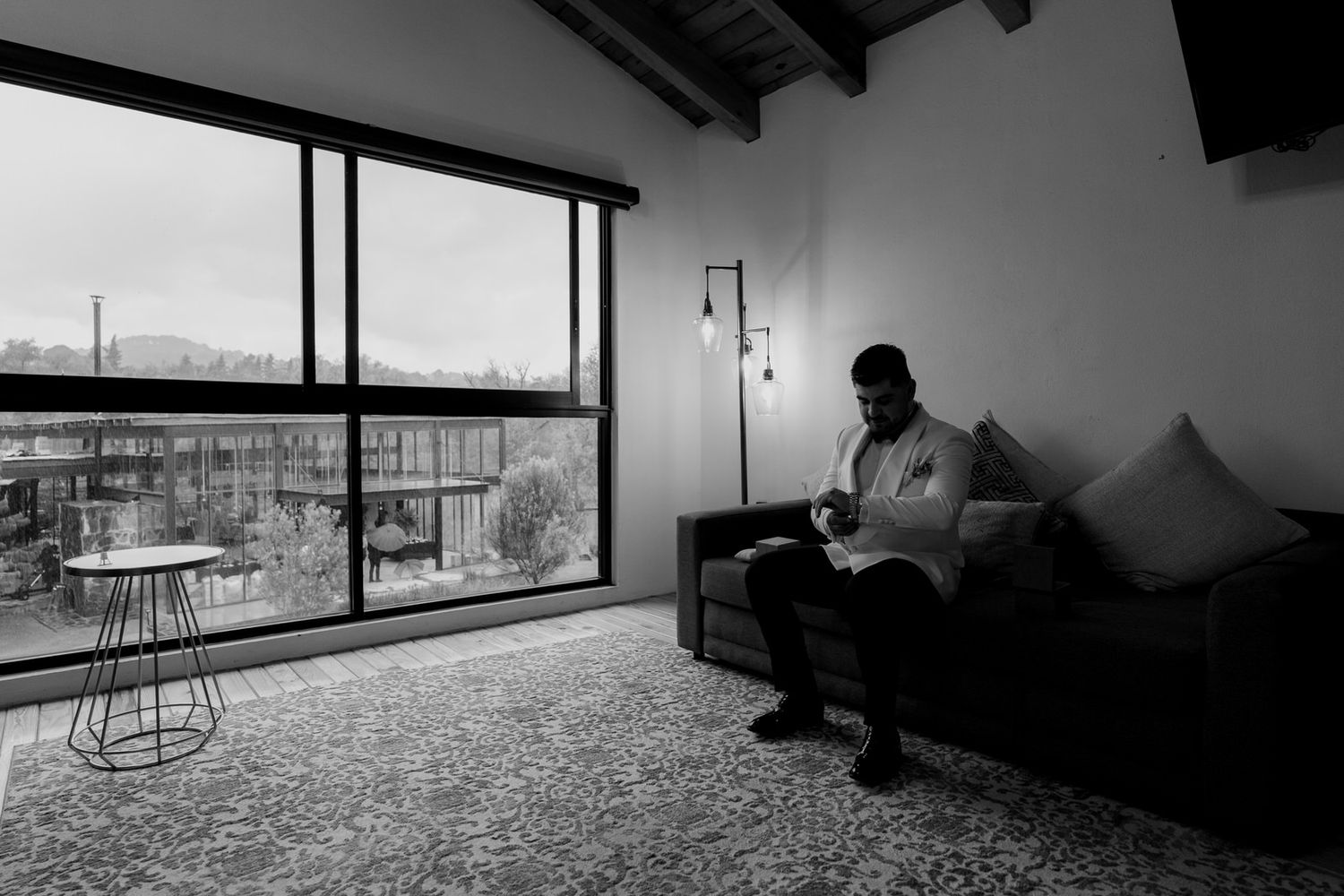 Black and white photo of person sitting in modern room with large windows and city view.