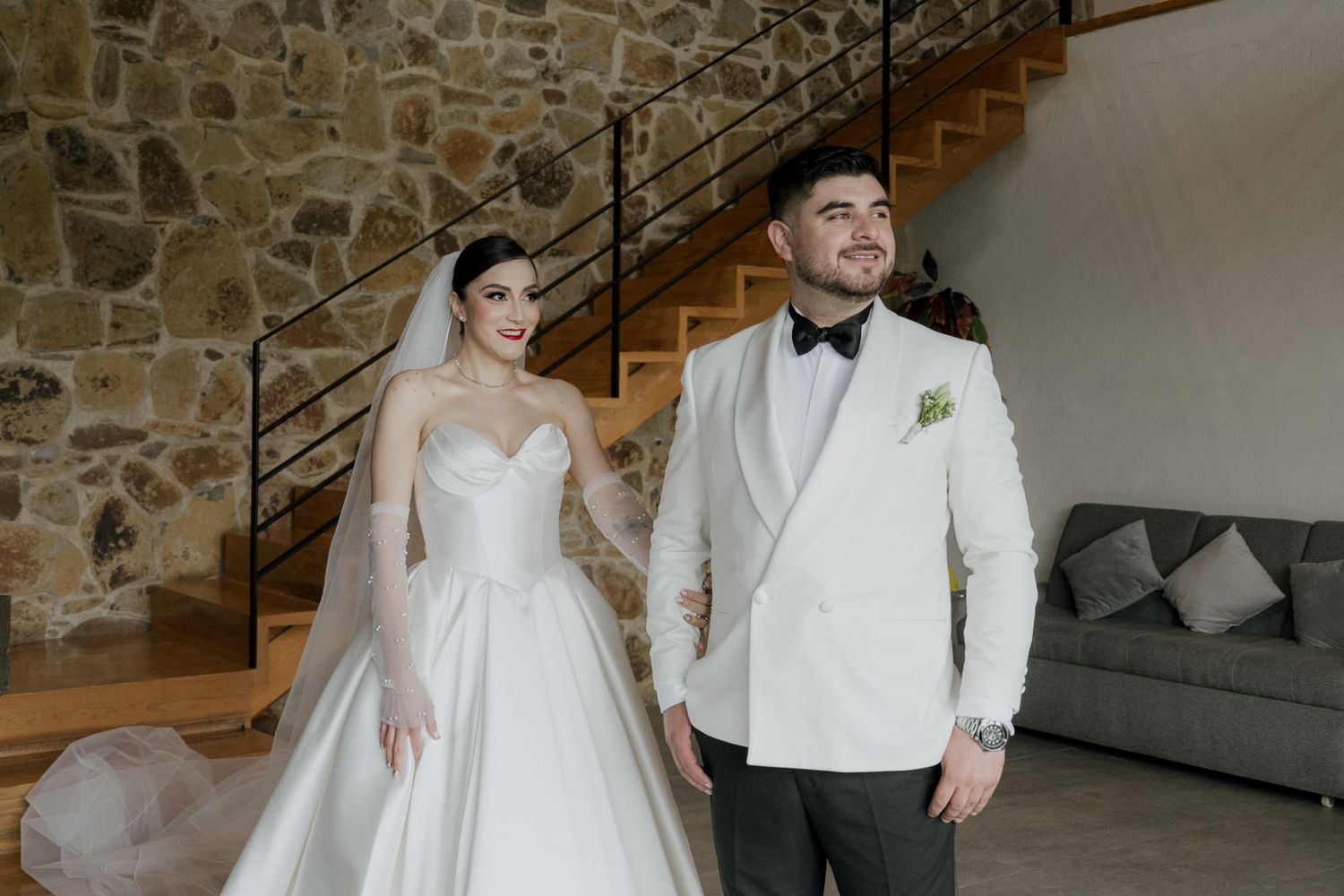 Elegant wedding couple posing in front of stone wall and wooden staircase.