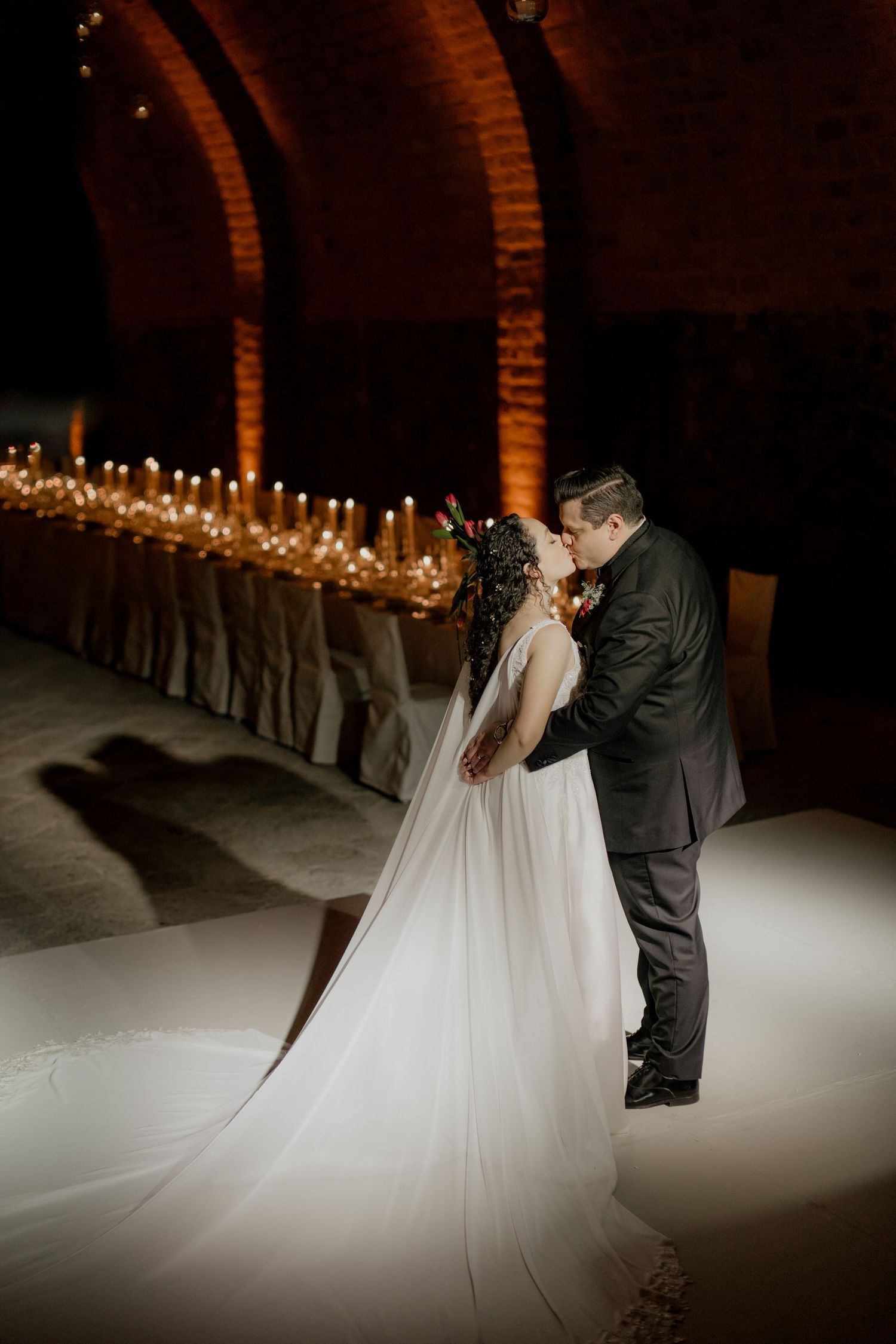 Couple shares an intimate moment in a dramatically lit brick tunnel with candles lining the walls.