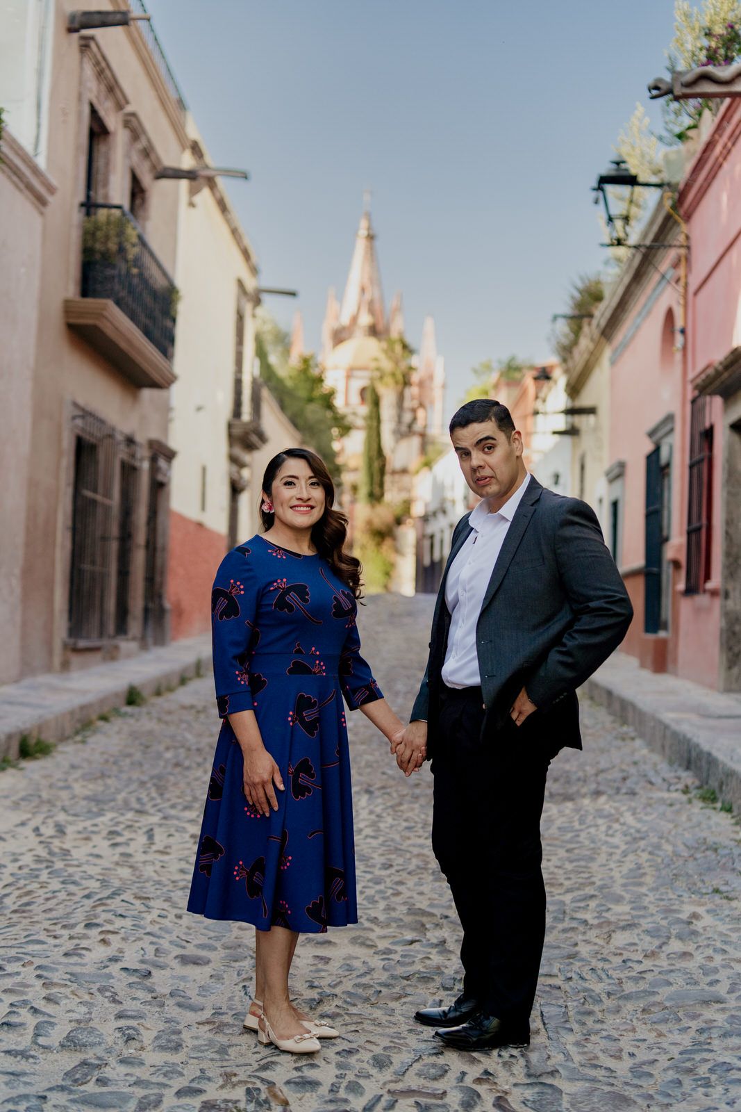 Couple stands together on a rustic cobblestone street in a historic Mexican town.