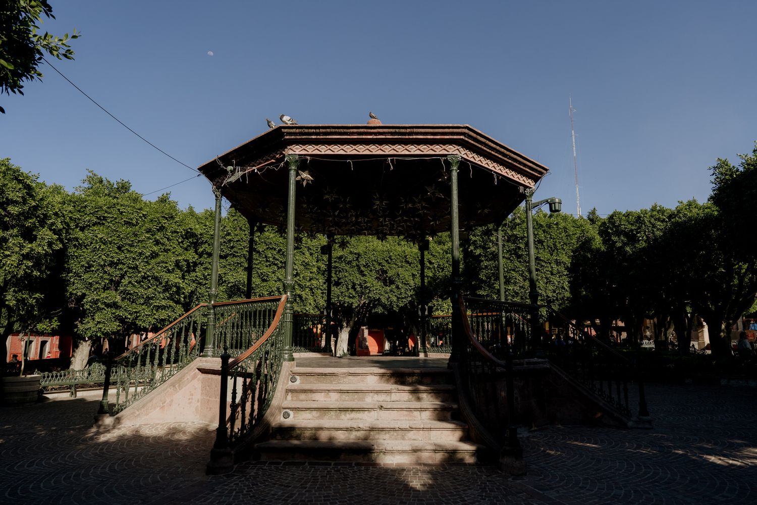 Panoramic view of a tree-lined park pathway with covered pavilion.