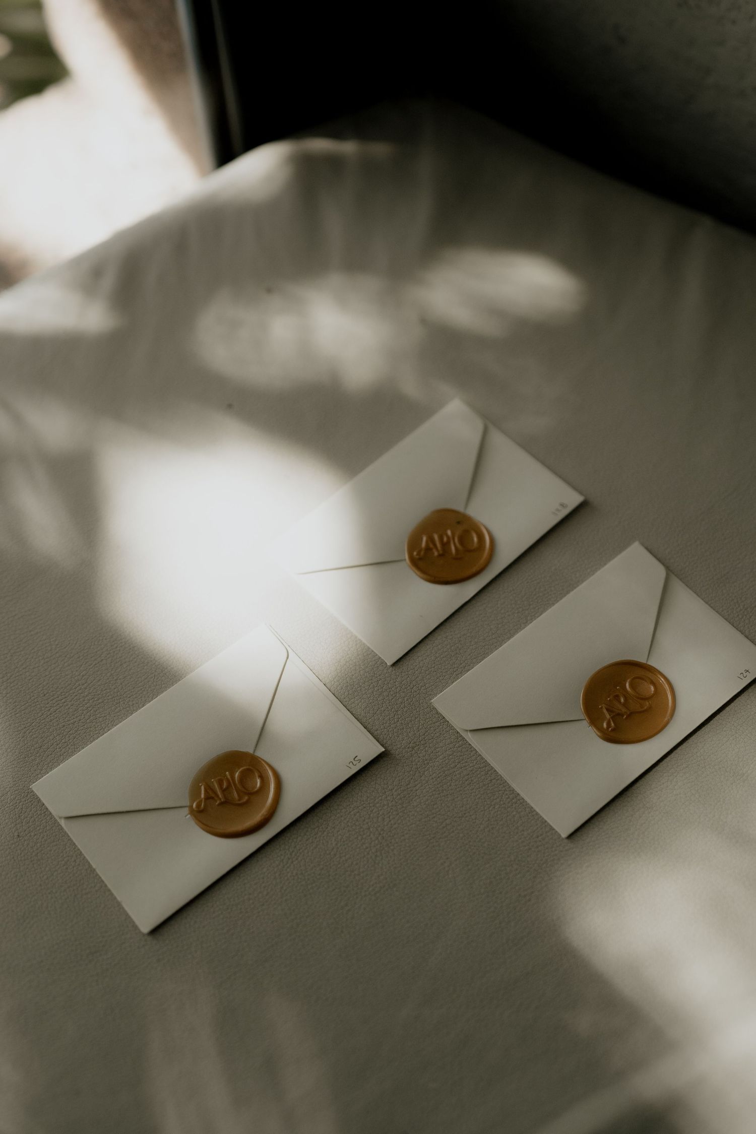 Three white wedding invitation envelopes sealed with gold wax stamps in natural light.