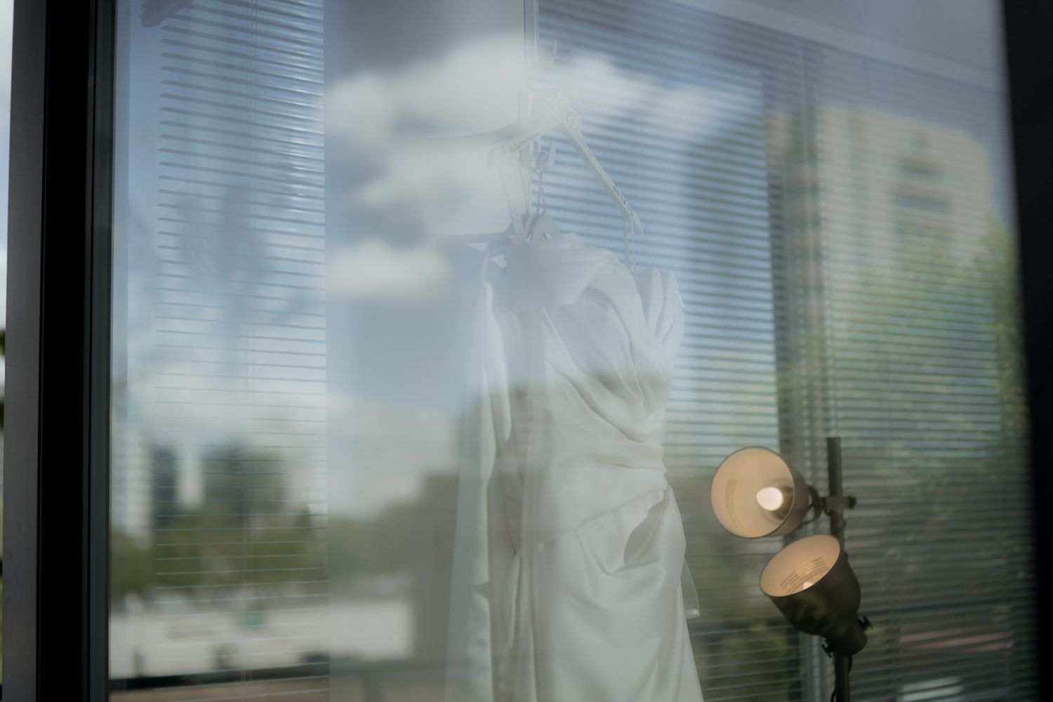 Artistic silhouette of a bride getting ready through window blinds with soft natural light.
