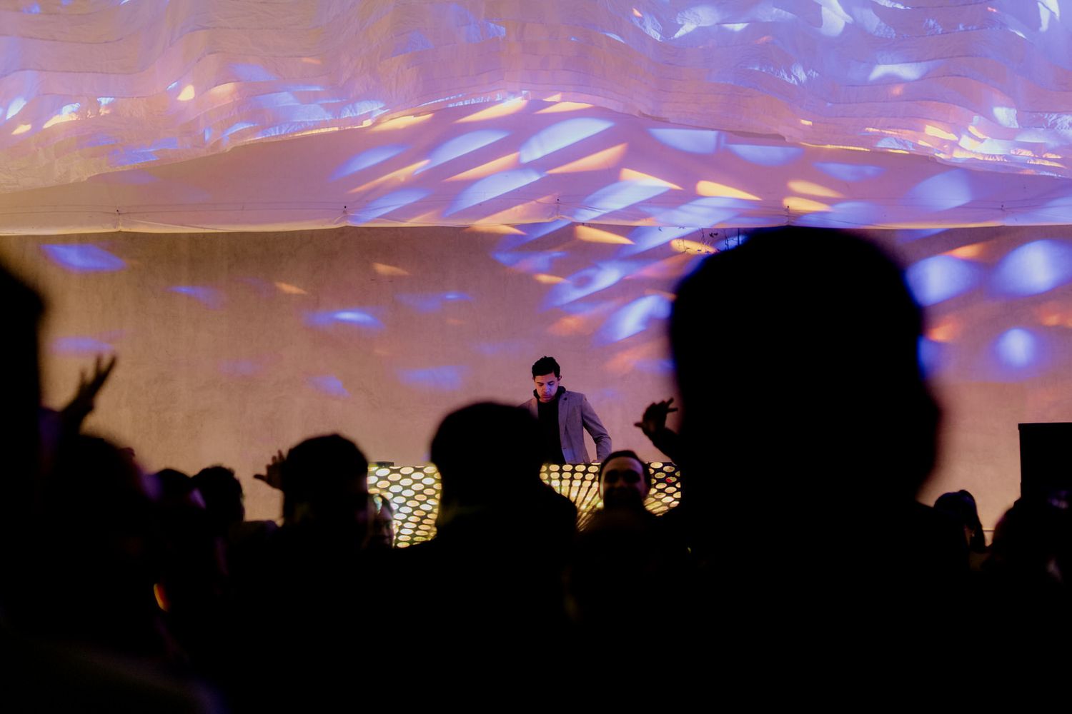DJ performing on stage with colorful light projections at a lively wedding party.