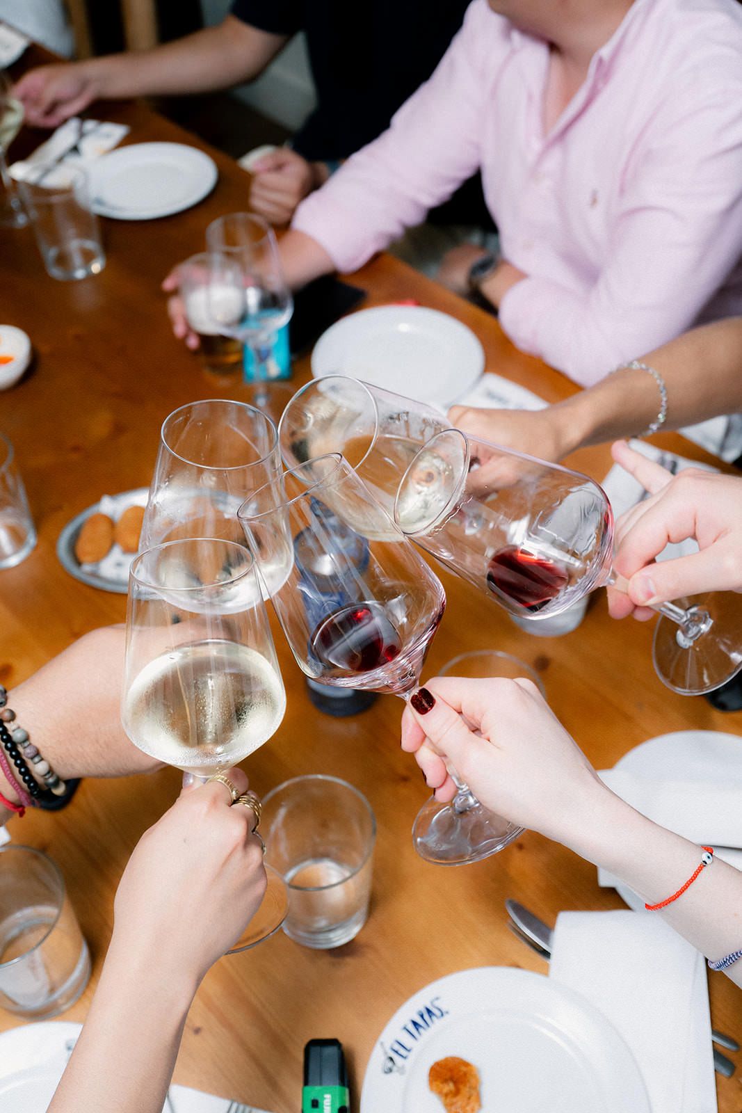 Hands pouring red wine into multiple wine glasses during a wine tasting event at a wooden table.
