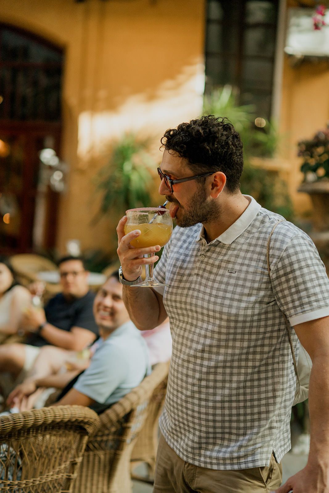 Person in checkered shirt enjoying a drink at an outdoor patio on a sunny afternoon.