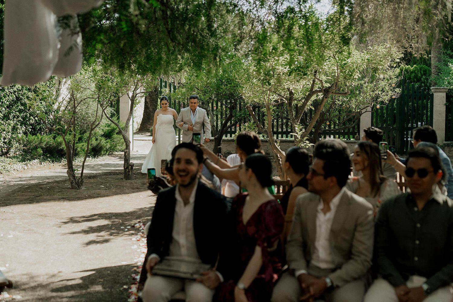 A group of guests seated at an outdoor garden wedding ceremony under trees.
