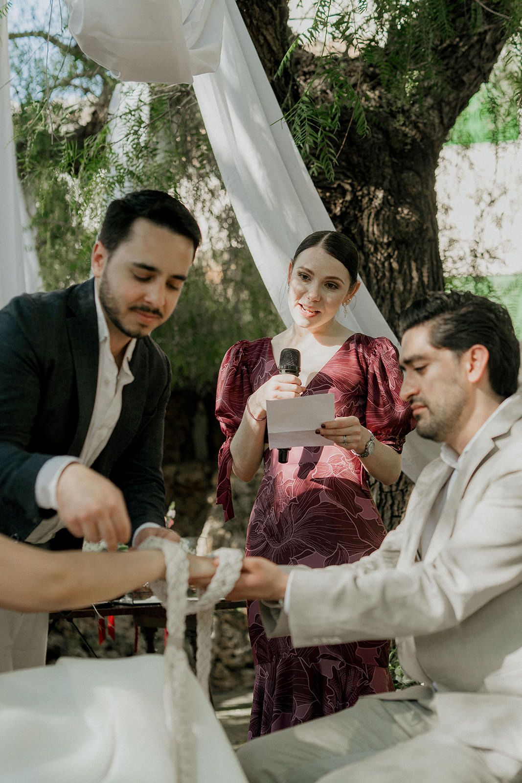 A couple shares a tender moment during their outdoor wedding ceremony under white fabric draping and trees.