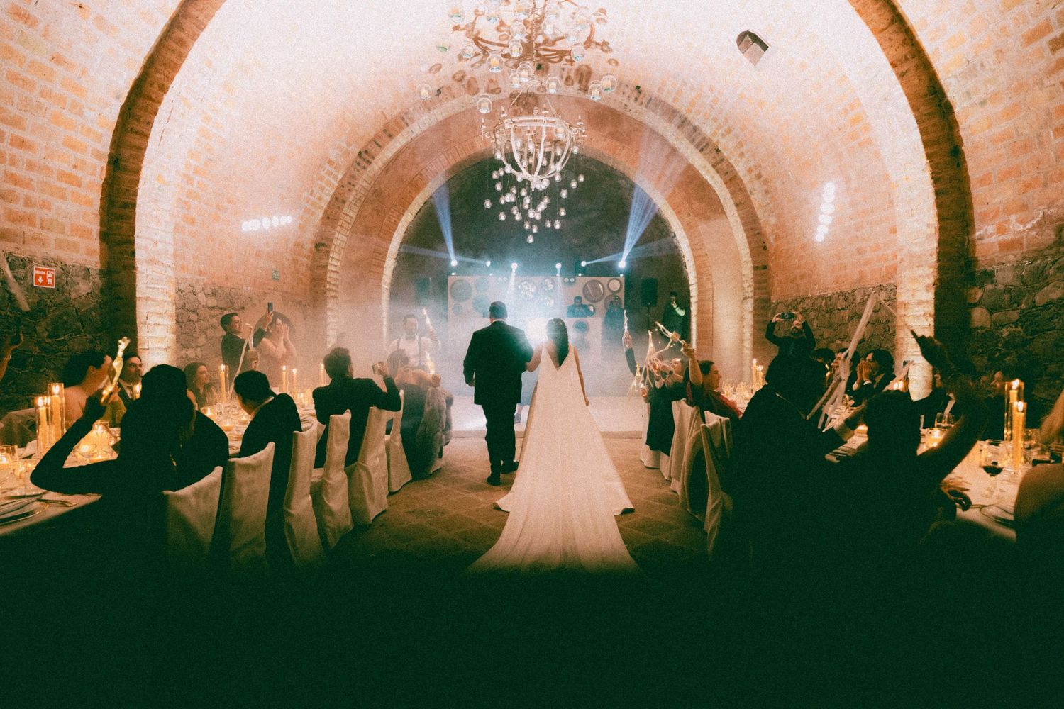 Wedding celebration in historic brick tunnel venue with silhouetted guests and dramatic lighting effects.