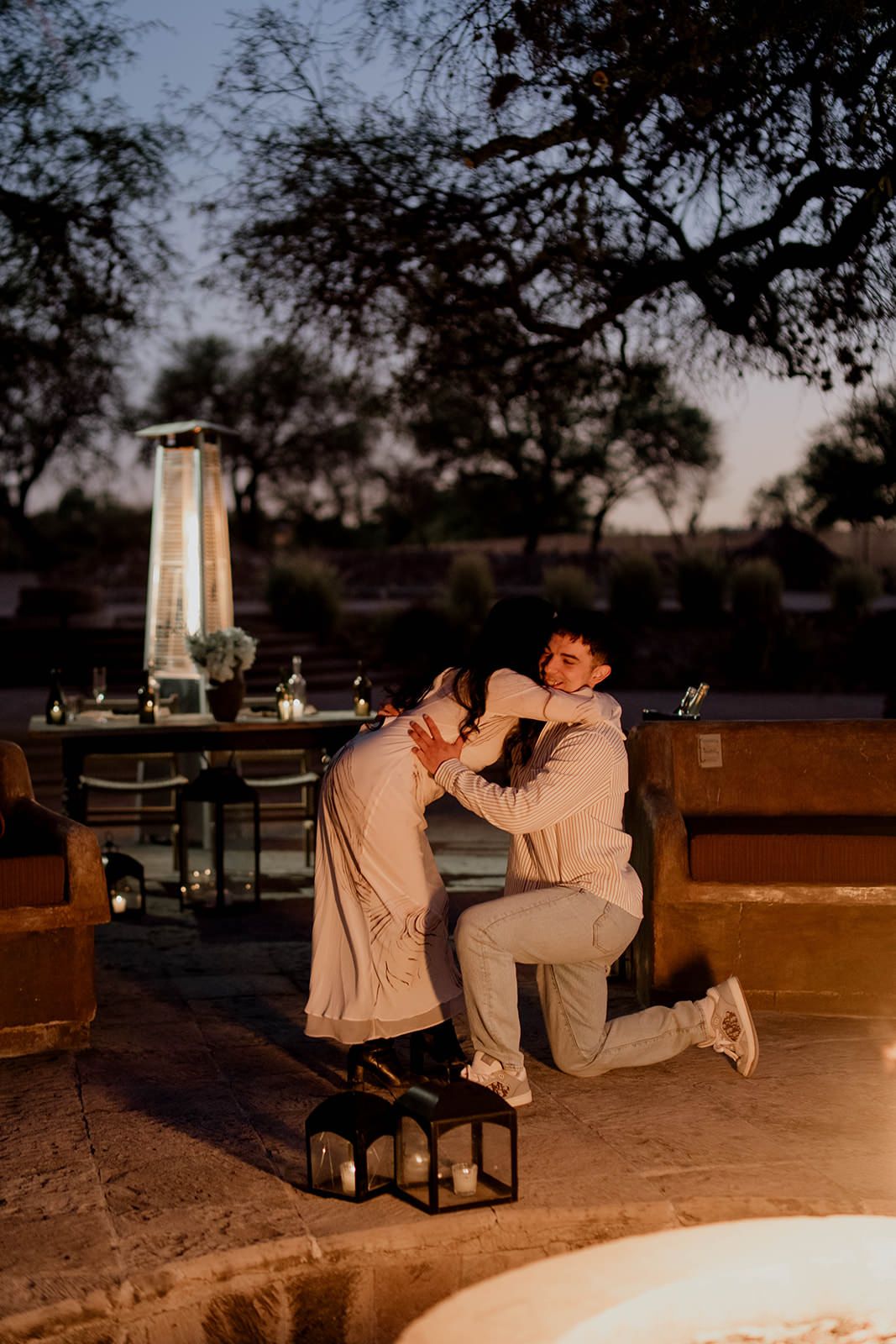 Two people share an emotional moment during a sunset proposal with lanterns nearby.