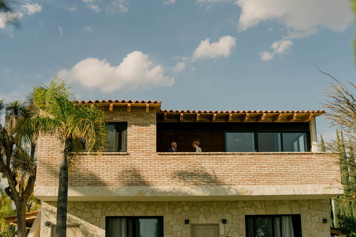 Modern stone building exterior with terrace under bright blue sky.