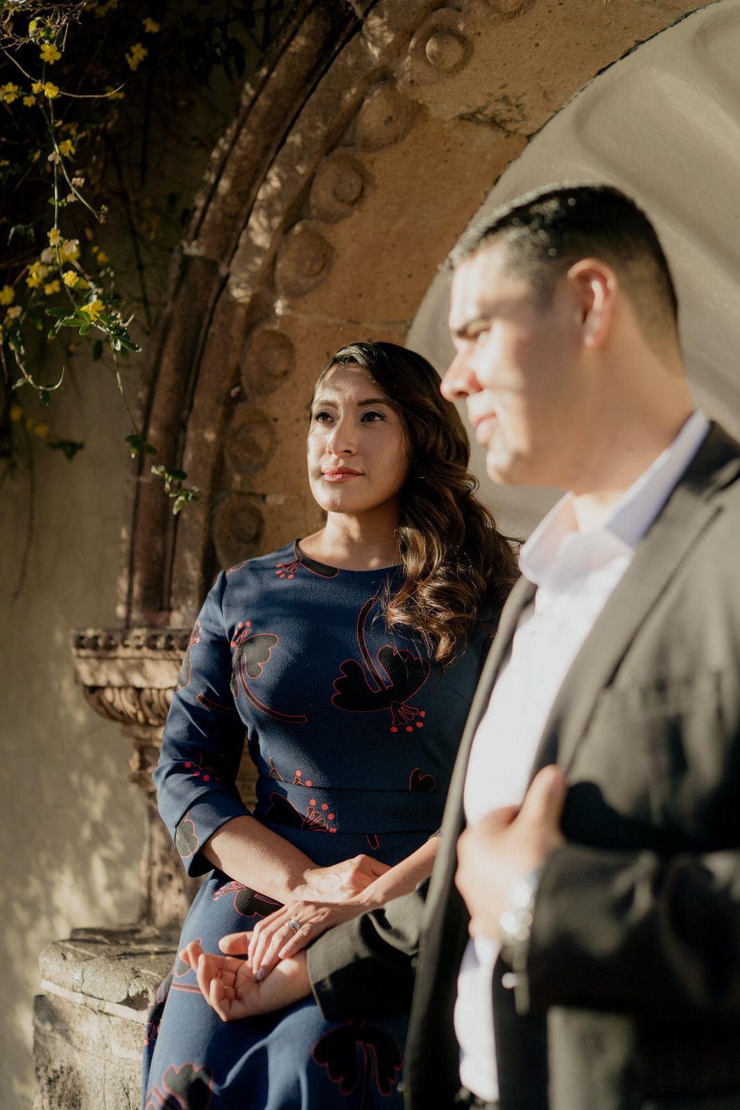 Couple shares an intimate moment under a historic stone archway with climbing vines.