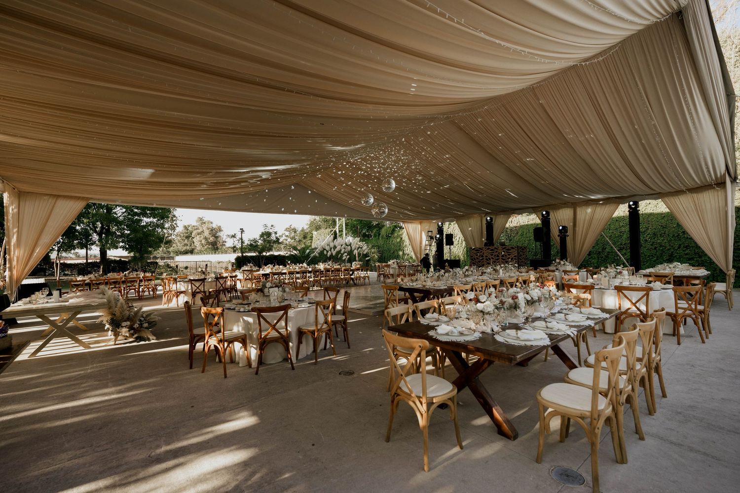Elegant reception tent with draped fabric ceiling and wooden cross-back chairs set for dinner.
